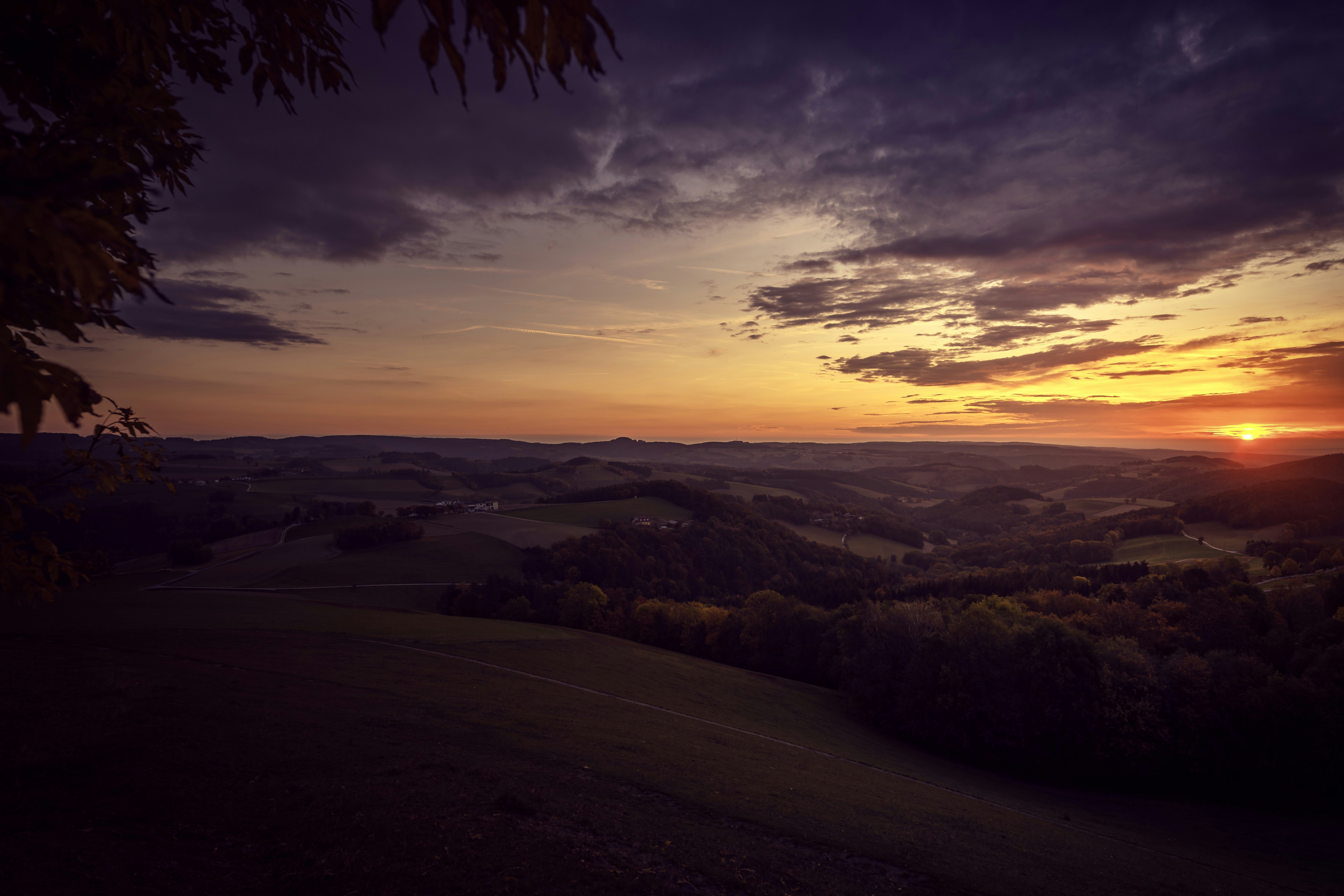 Rolling hills under a dark cloudy sky with a low sun on the horizon