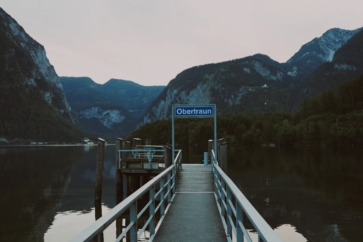 A wooden pier with an Obertraun sign on the Hallstätter See, with cliffs and forest behind