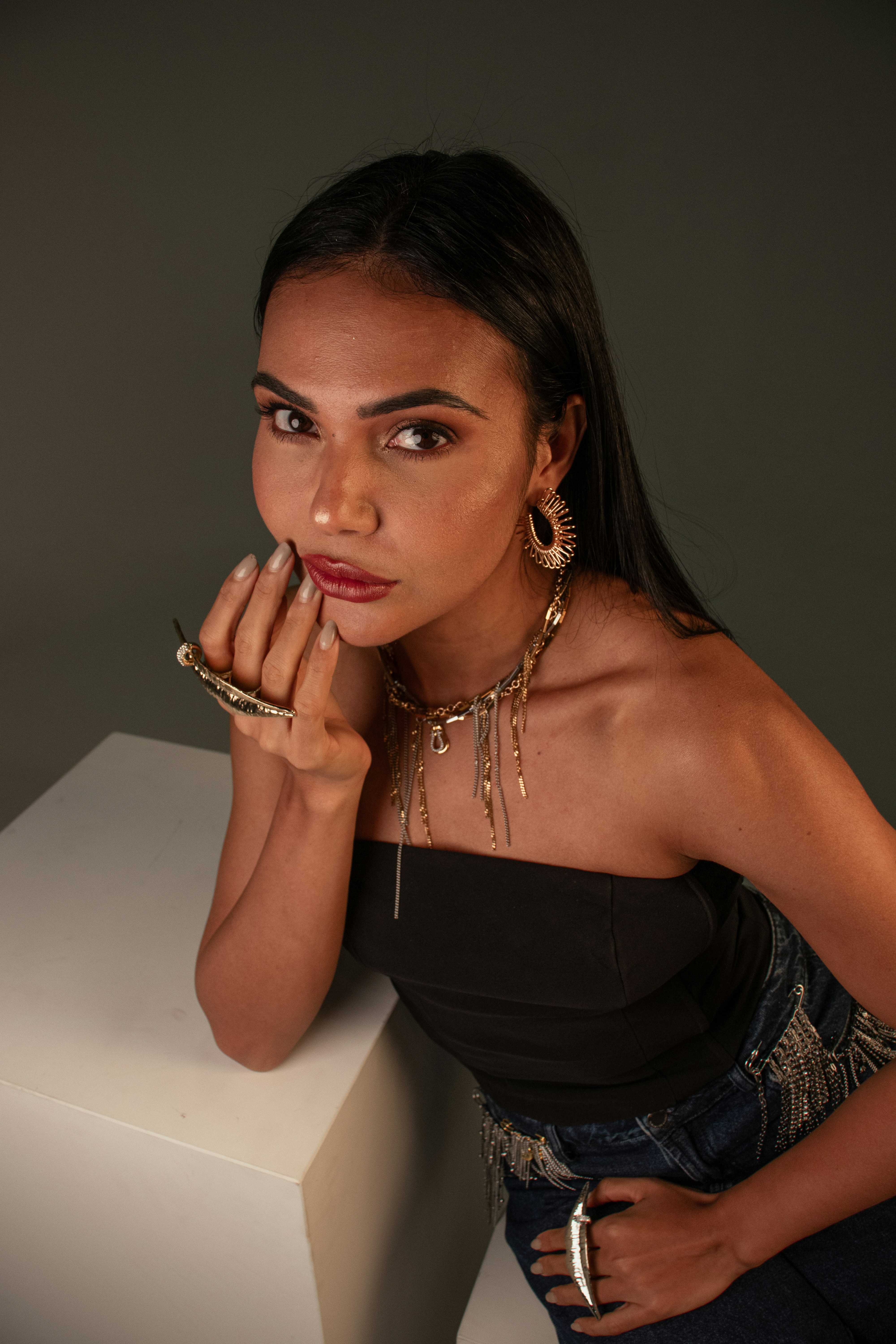 A woman in a black tube top and jeans wearing layered gold jewelry