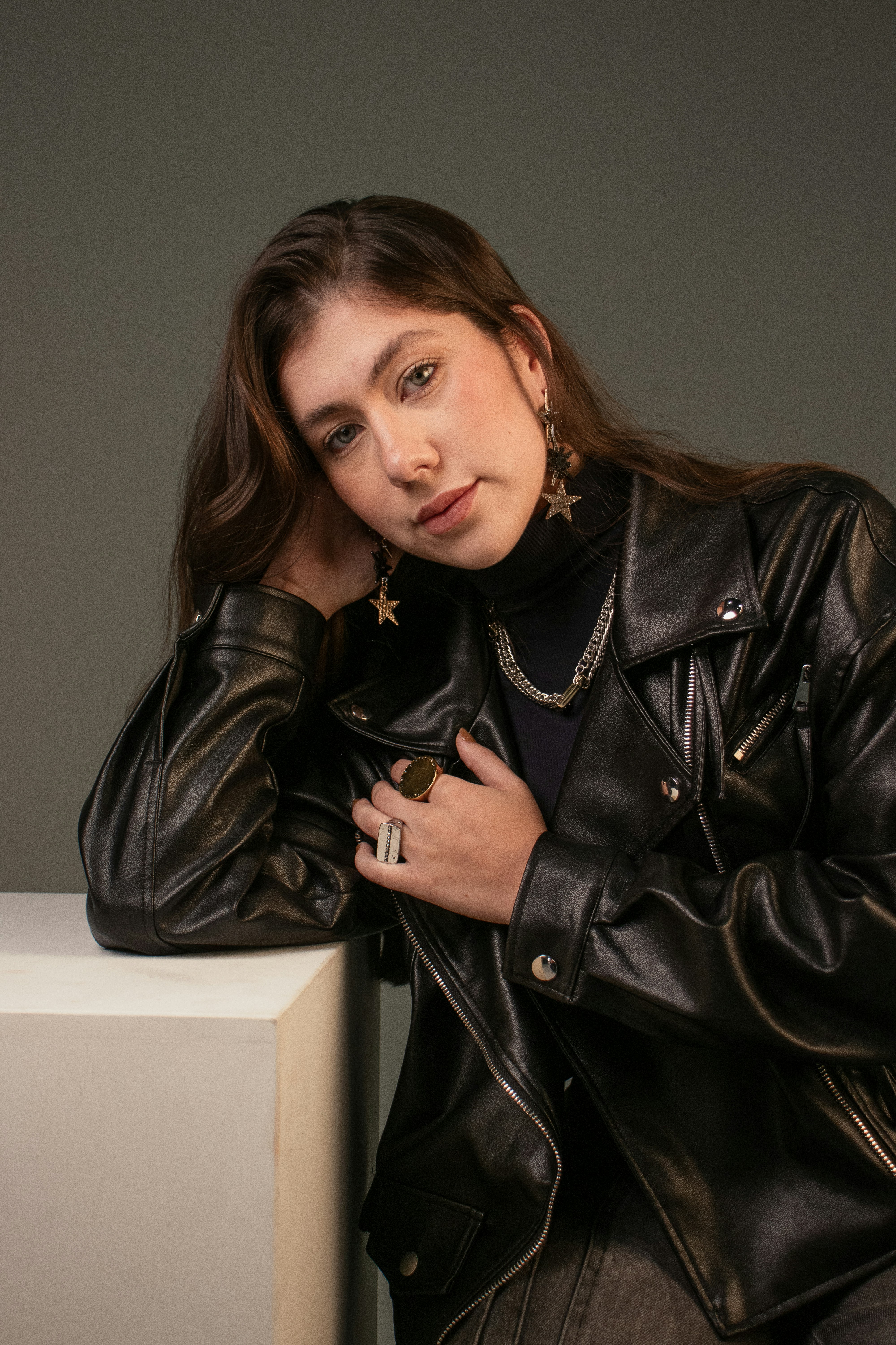 A woman in a black leather jacket and turtleneck leaning on a white block
