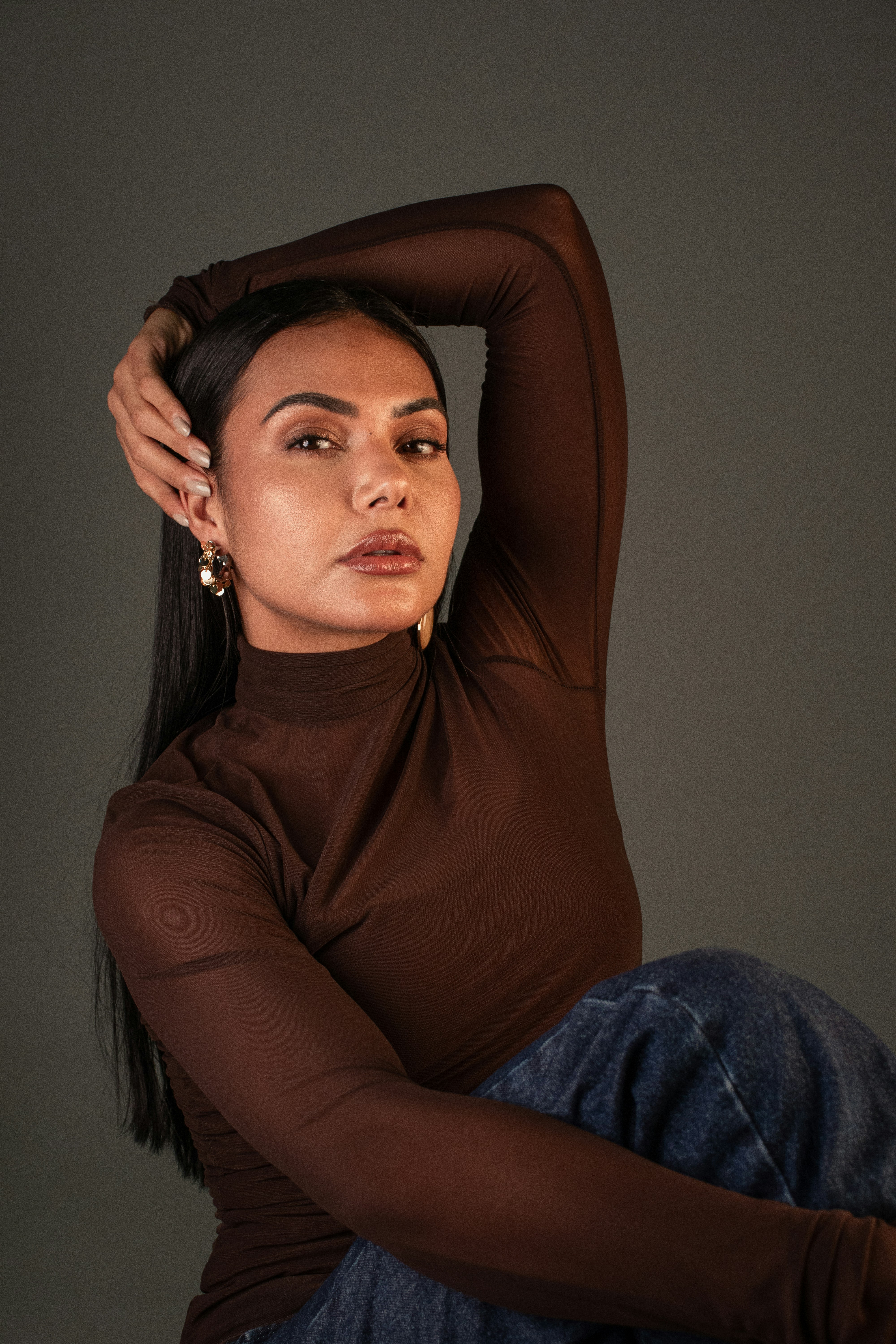 A woman with long dark hair wearing a brown long-sleeved top and blue jeans