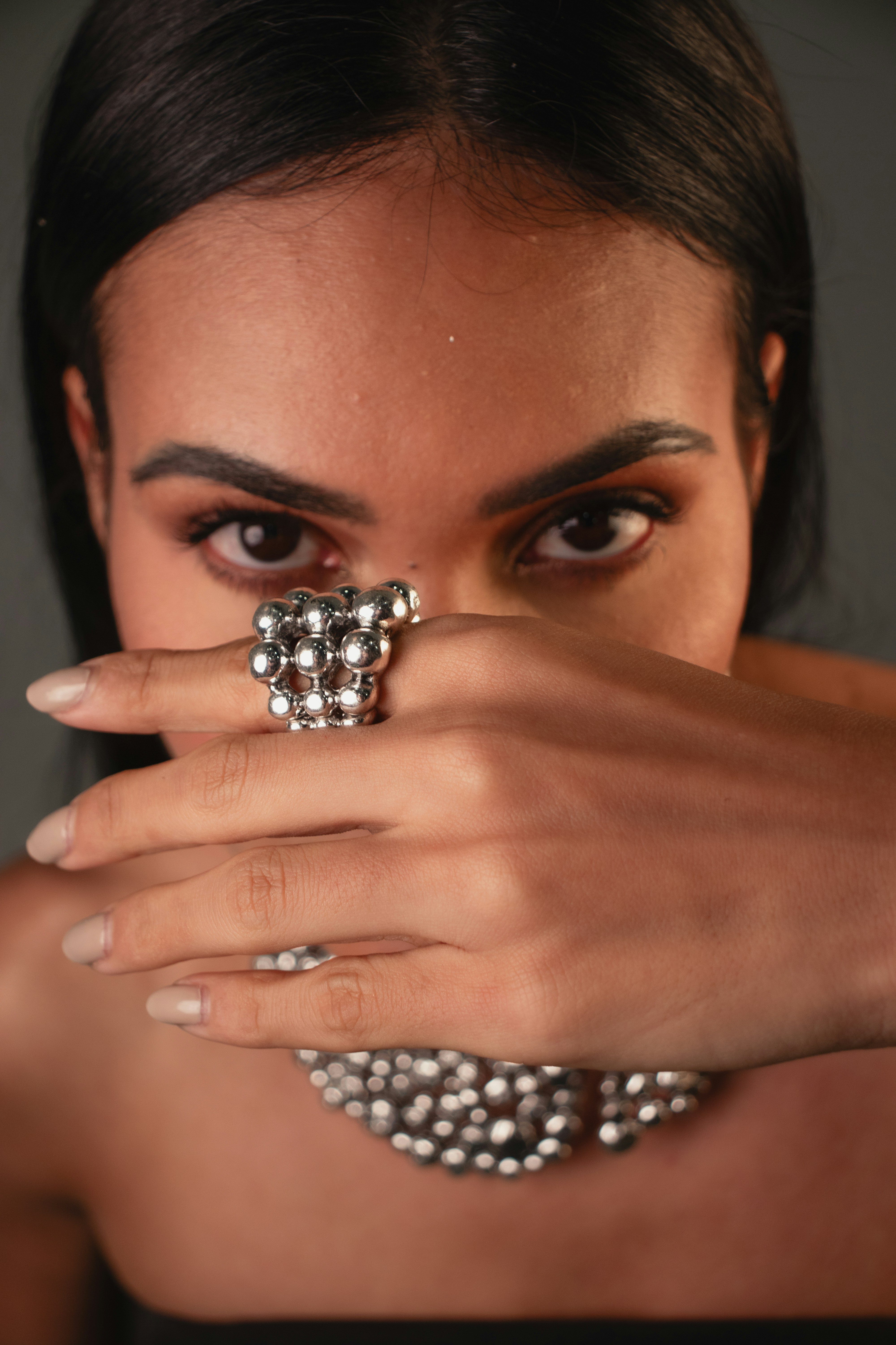 A person covering their face with a hand wearing a silver beaded ring