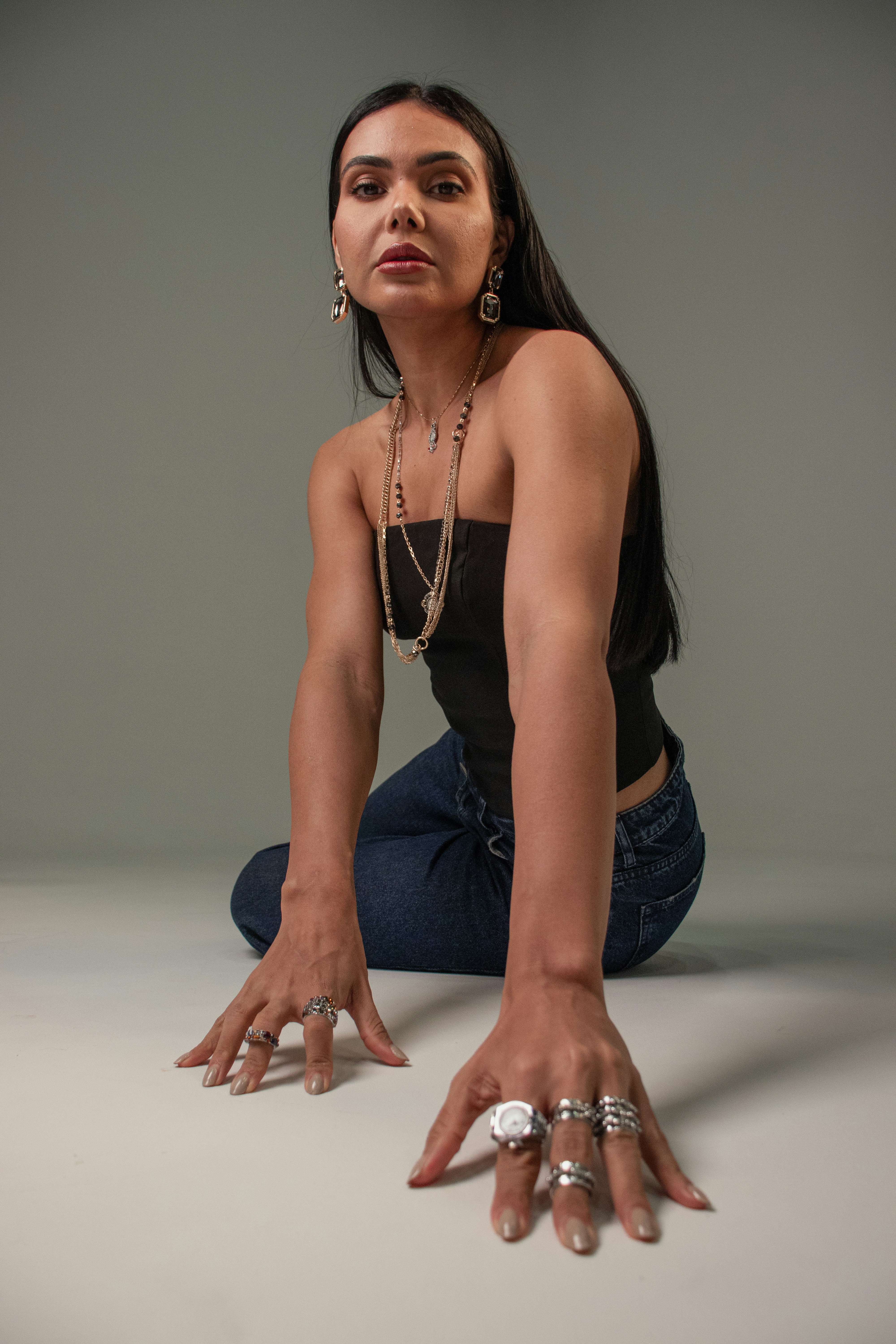 A woman in a black tube top and jeans kneeling on a grey floor