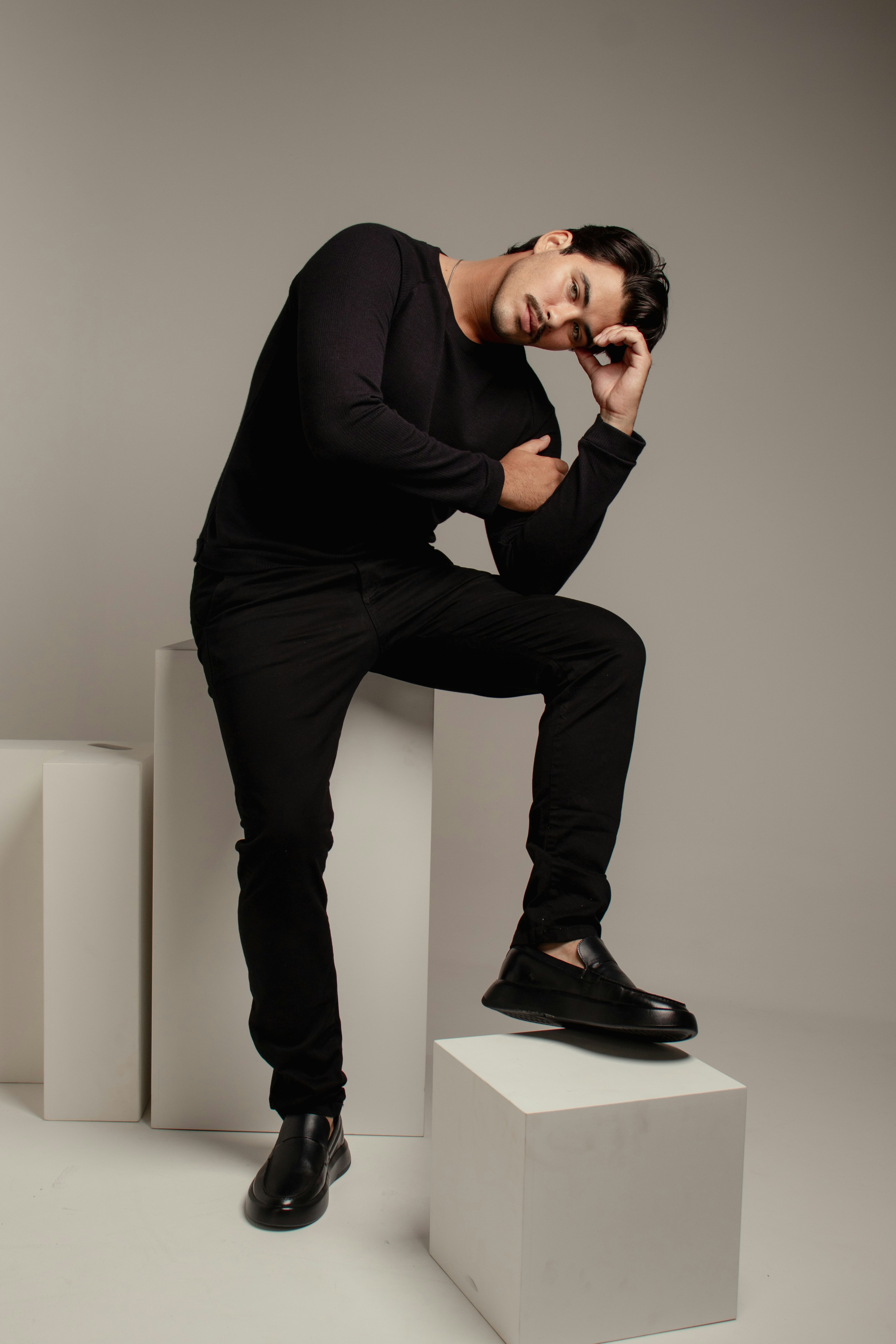 A man in a black long-sleeved shirt and trousers posing on white blocks