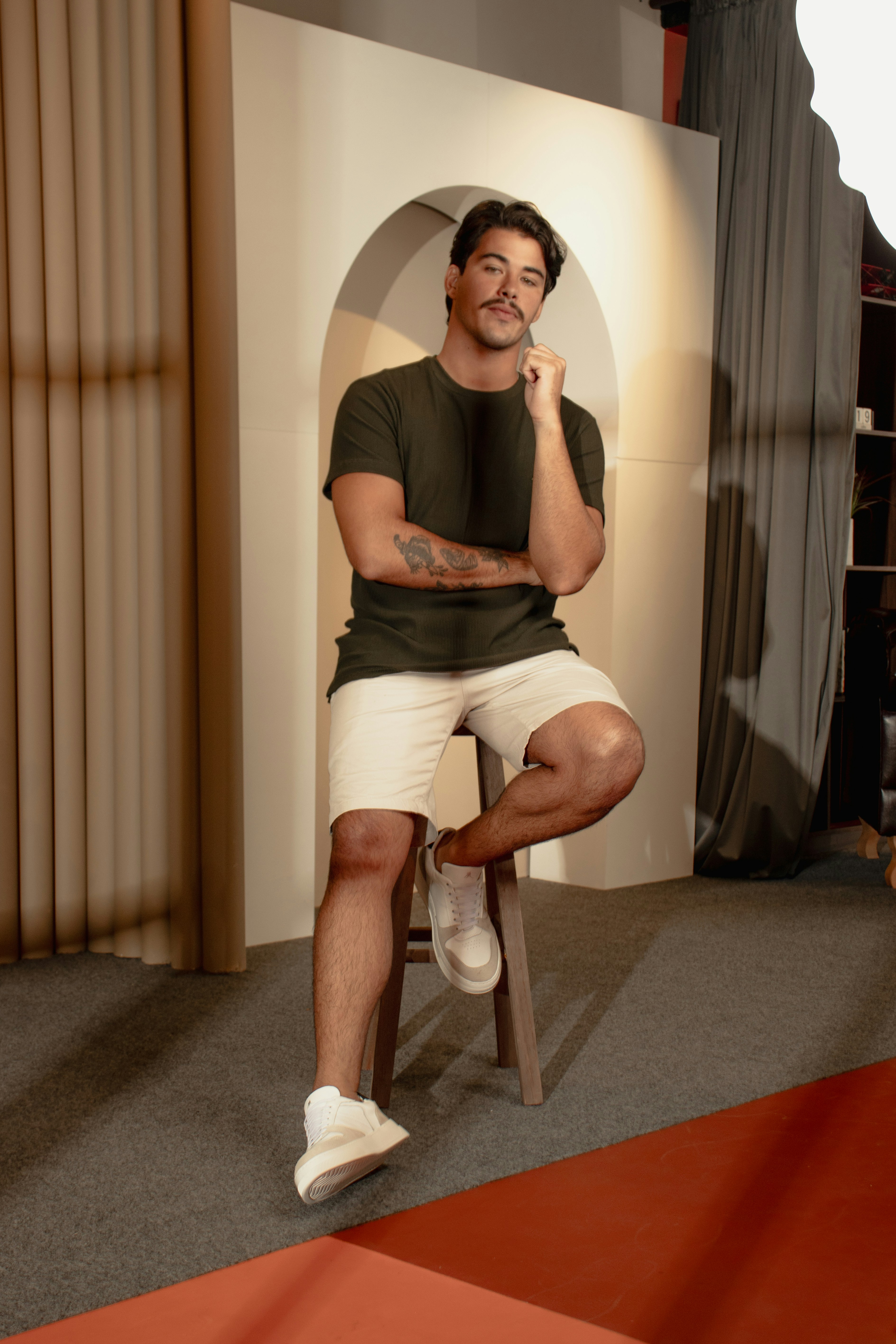 A man with a mustache in a dark green t-shirt sitting on a stool