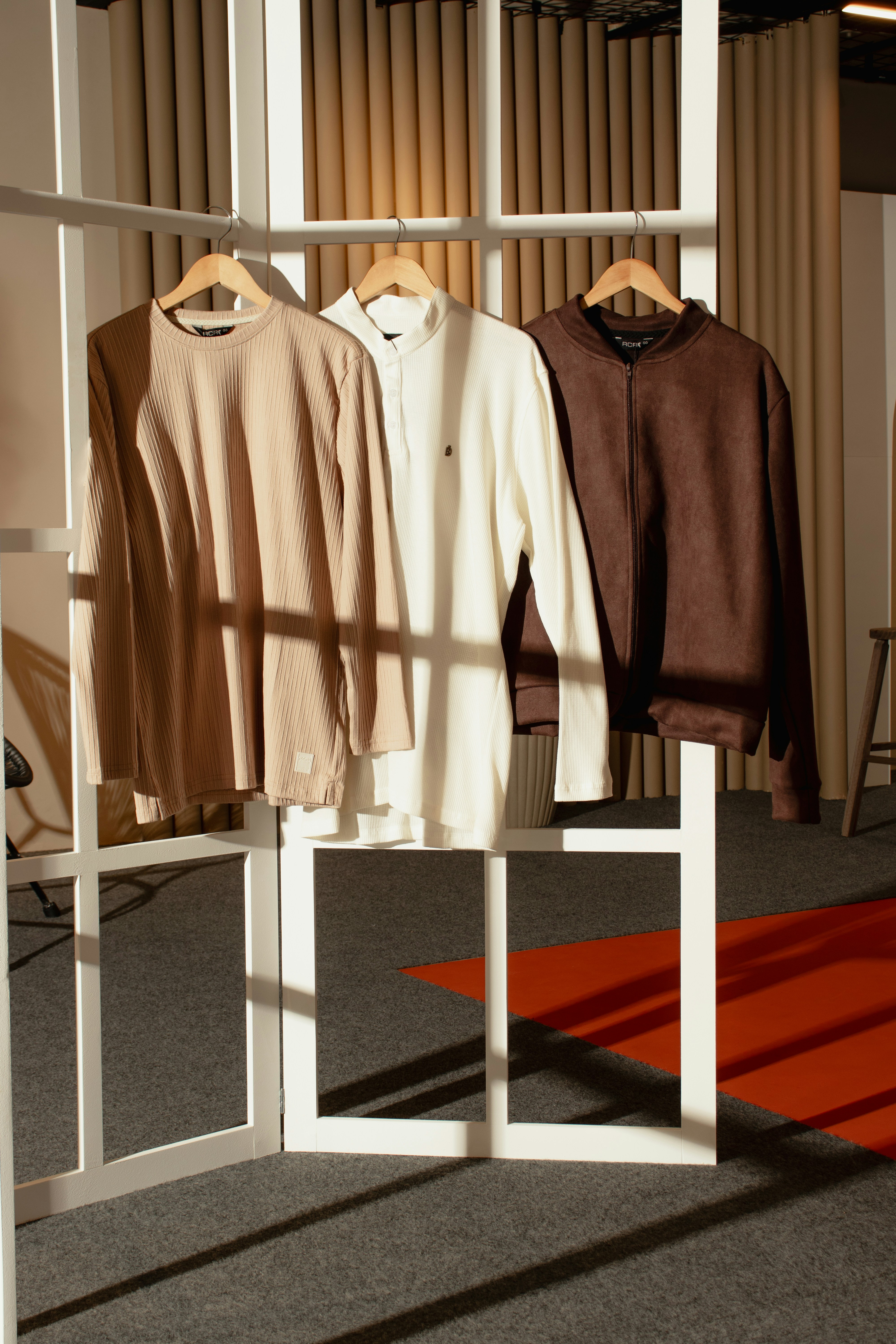 Three shirts hanging on a white room divider in a sunlit studio