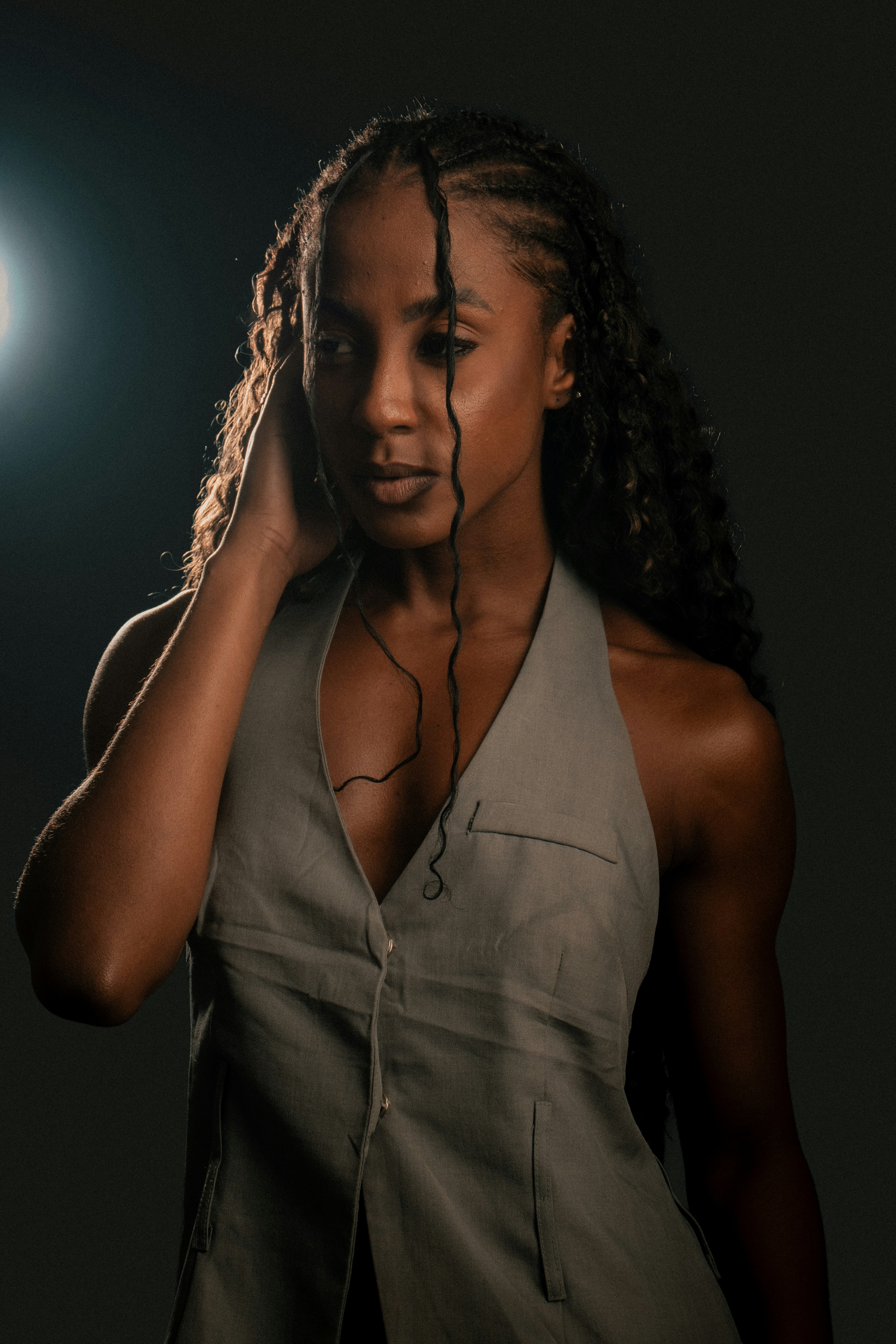 A woman with long braided hair wearing a grey vest against a dark background