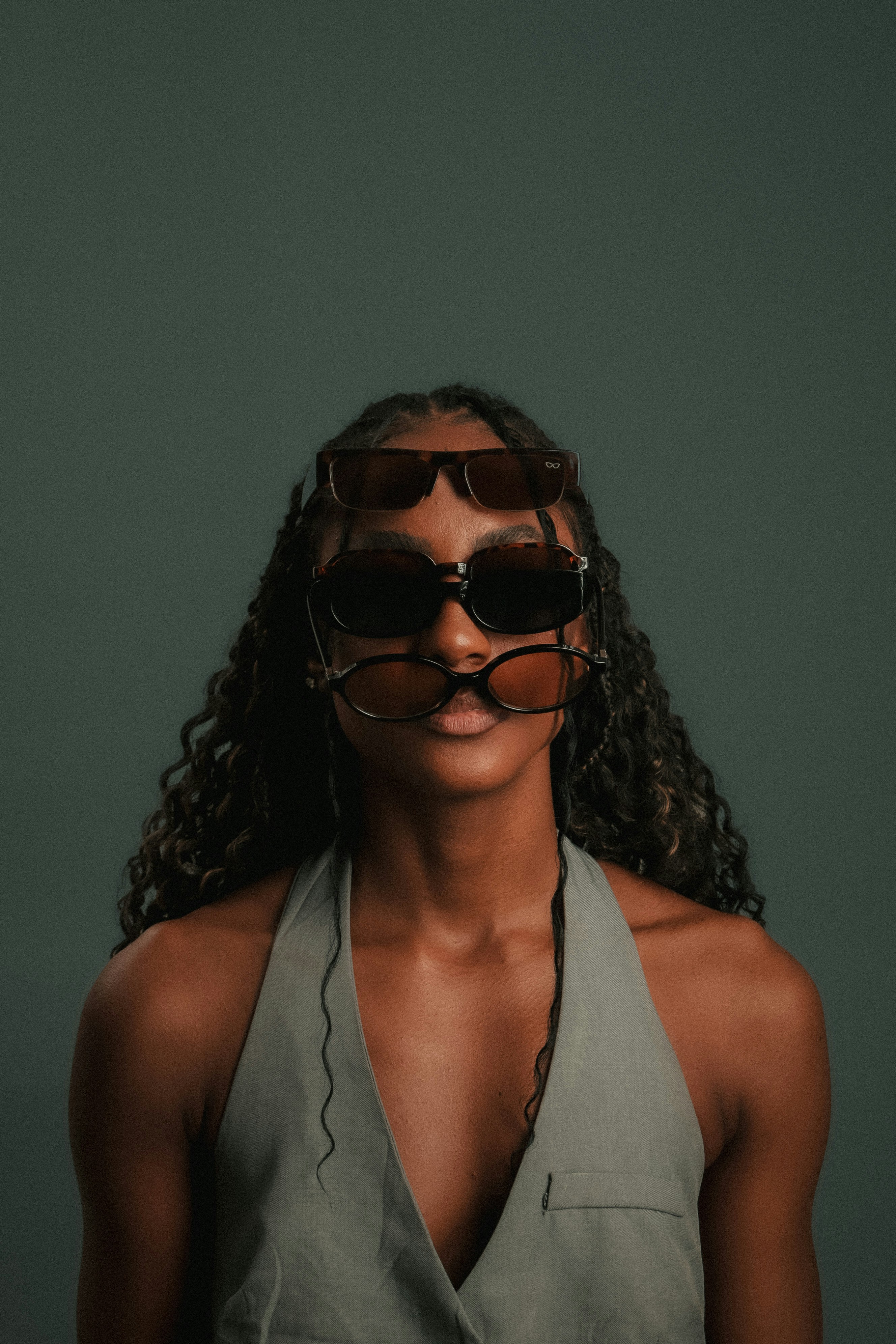 A person with long curly hair wearing three pairs of sunglasses stacked vertically