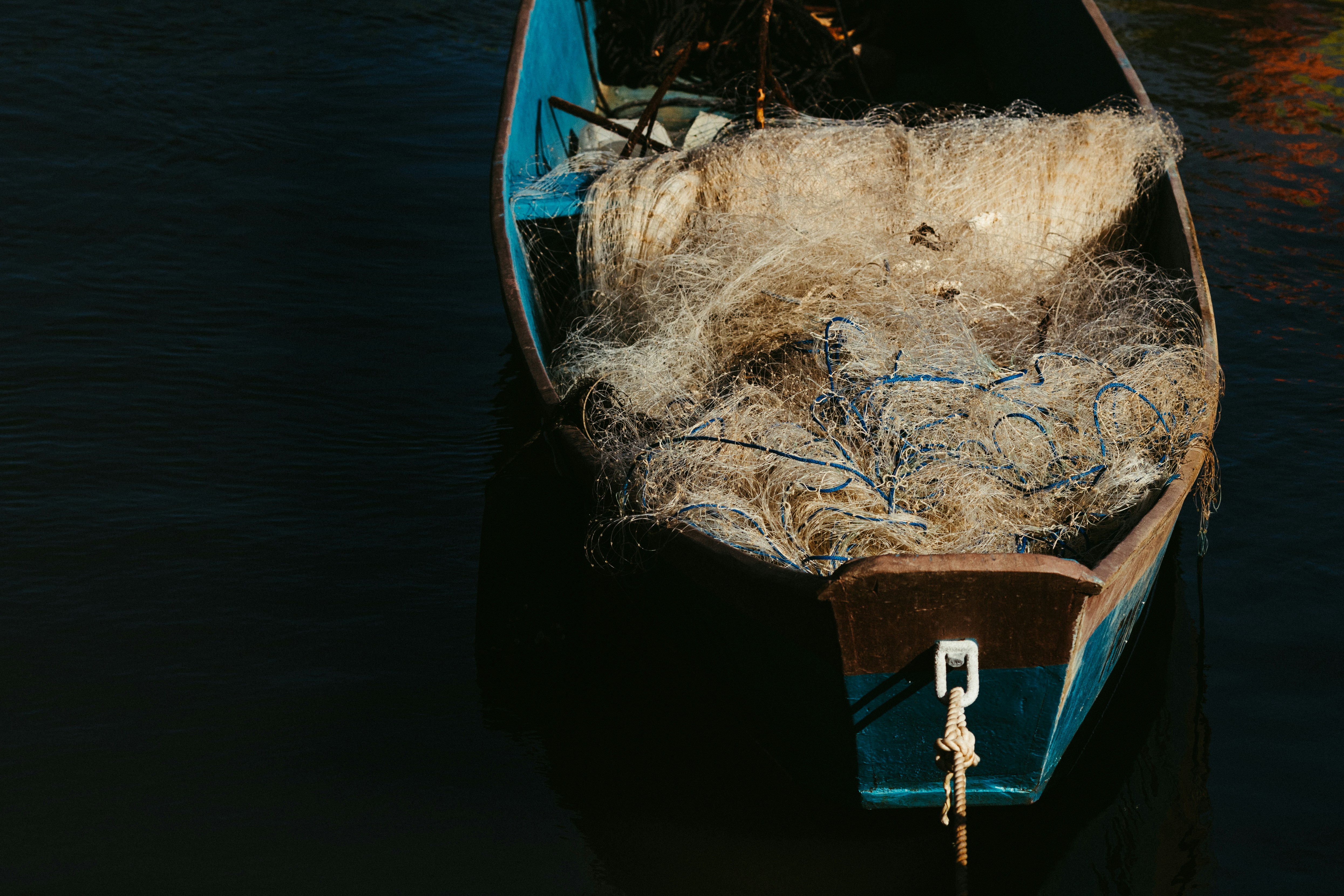 Un pequeño barco azul lleno de redes de pesca enredadas sobre aguas oscuras