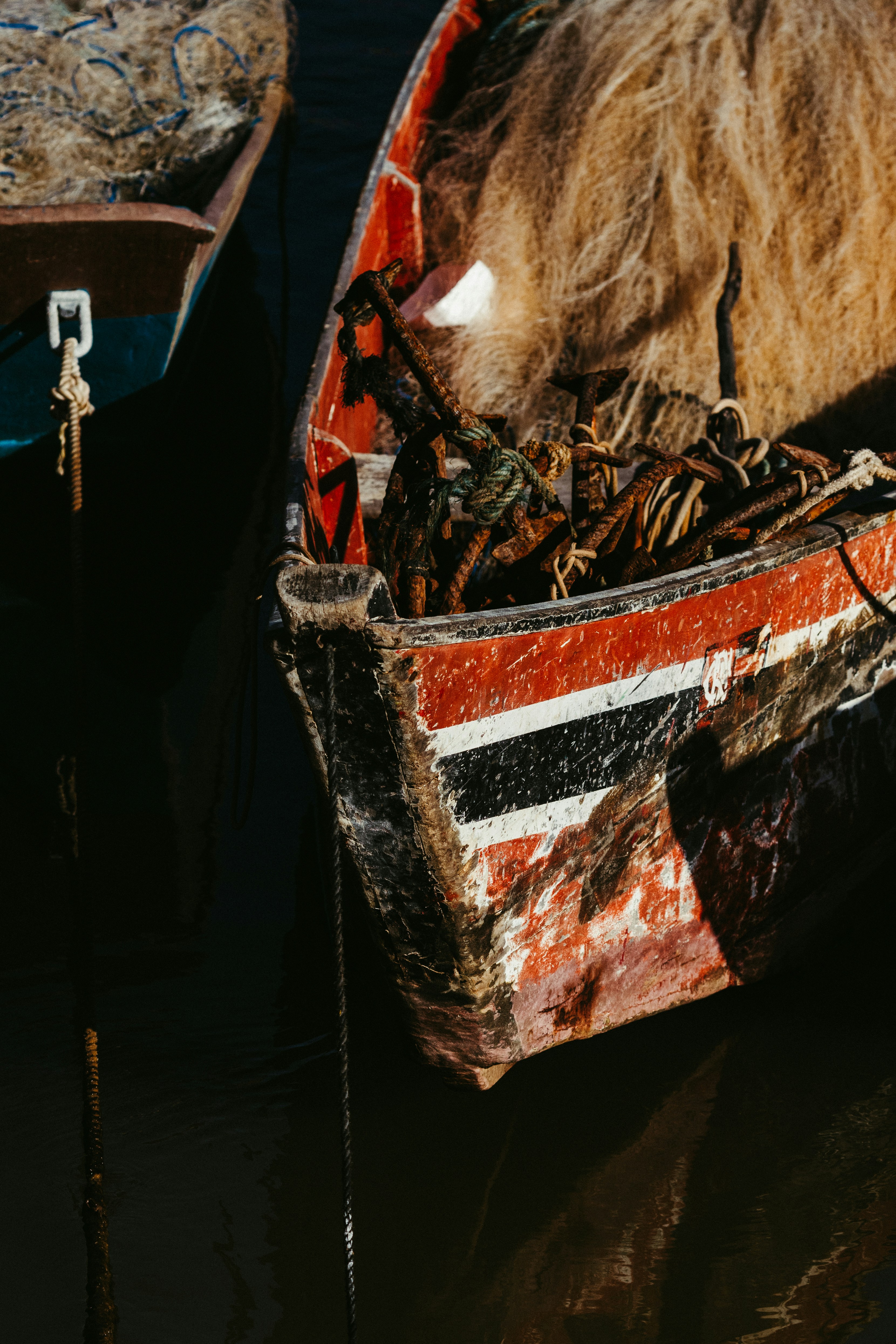 Un barco pesquero de madera roja y negra desgastada lleno de anclas metálicas oxidadas