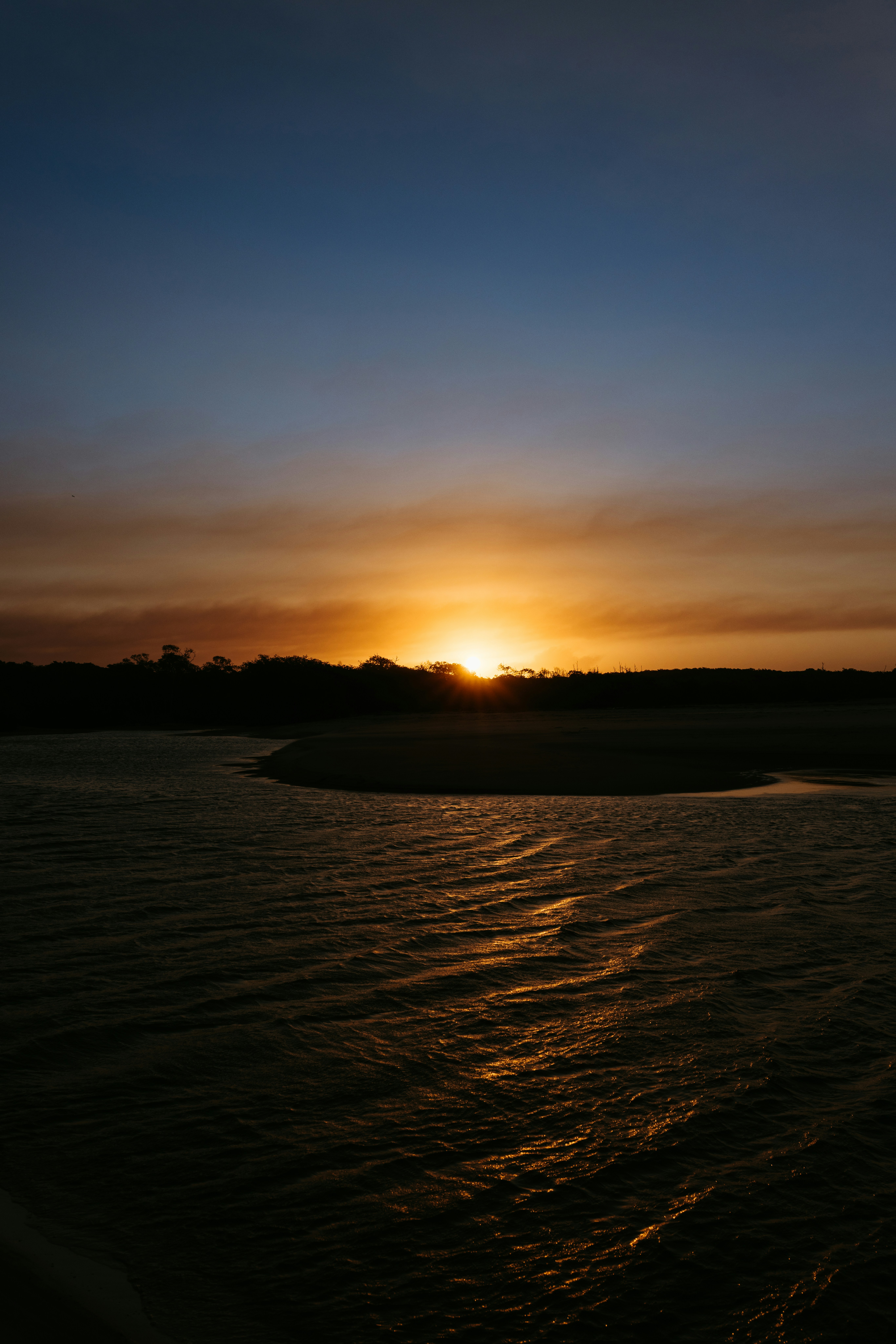 Sol bajo brillando tras una línea de árboles oscura sobre el agua ondulante