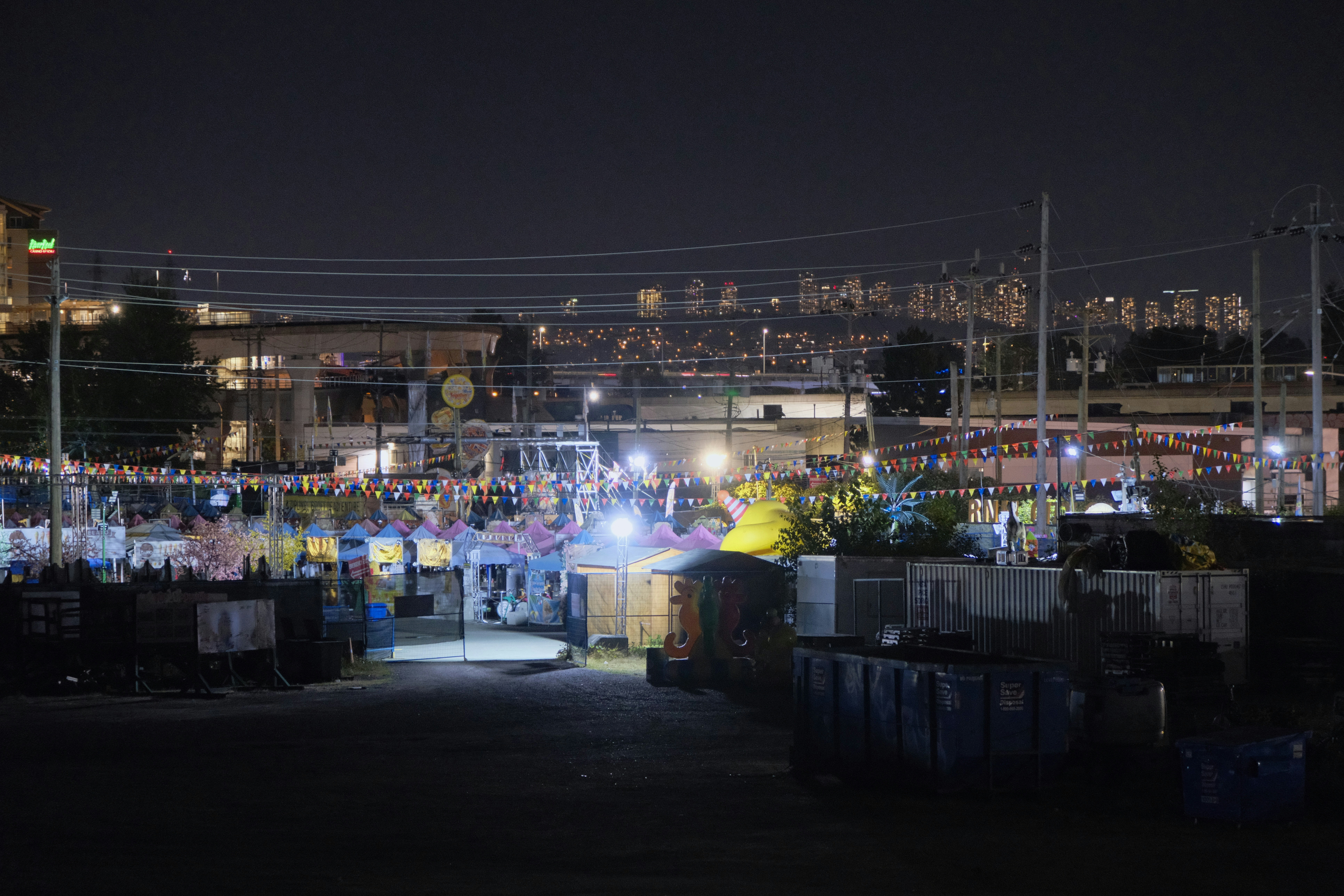 A night carnival with colorful bunting and illuminated stalls under a city skyline