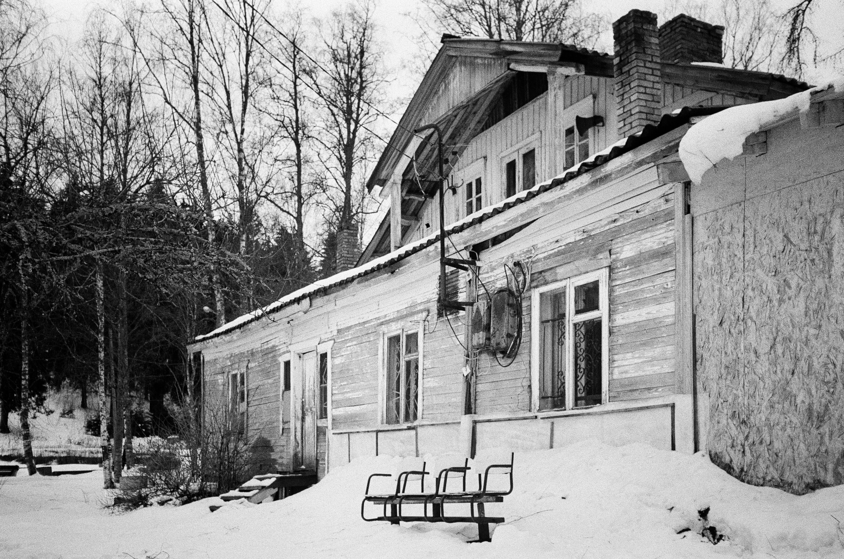 Una casa di legno consumata dal tempo con una panchina di metallo nella neve profonda