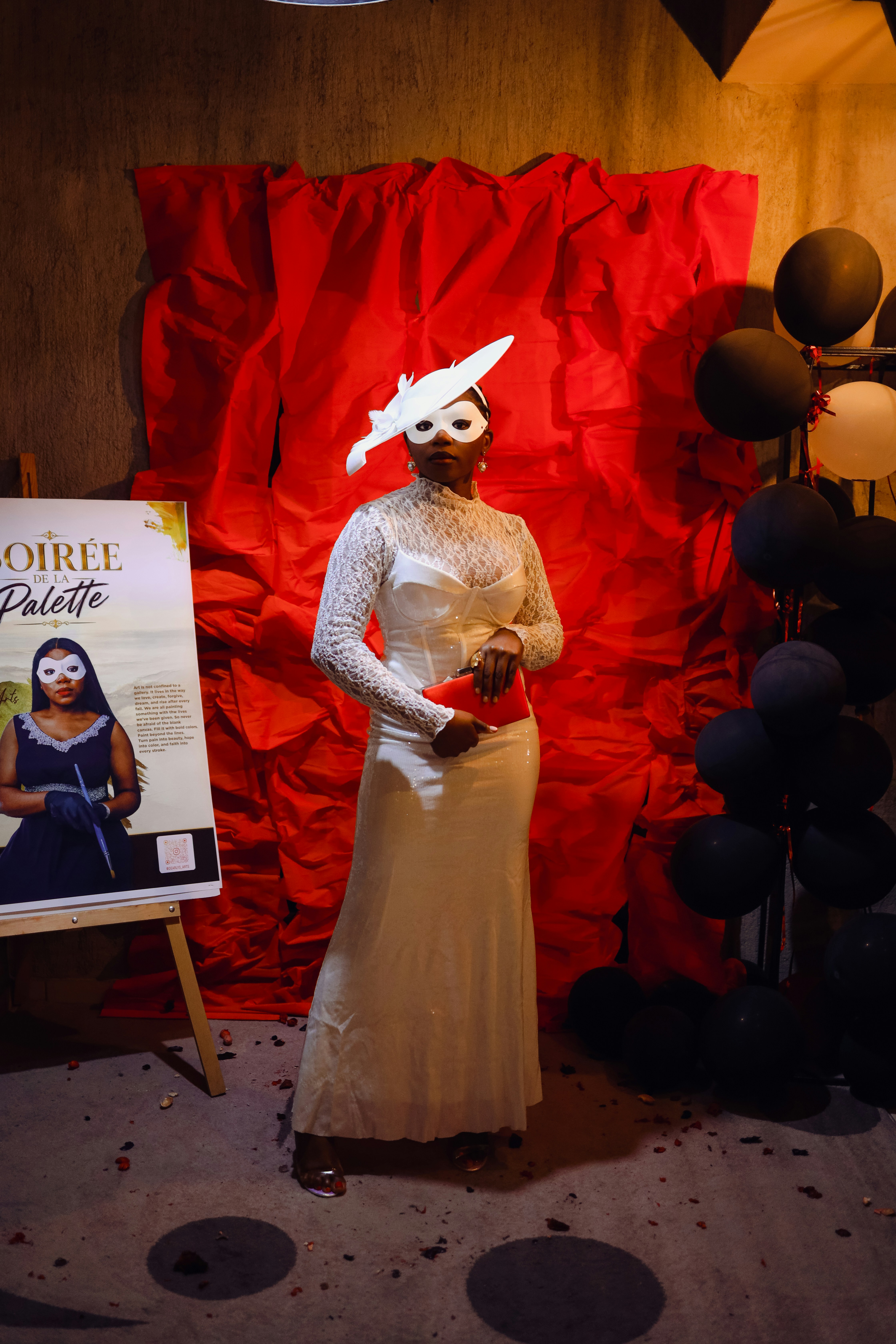A woman in a white lace dress and mask holding a red clutch