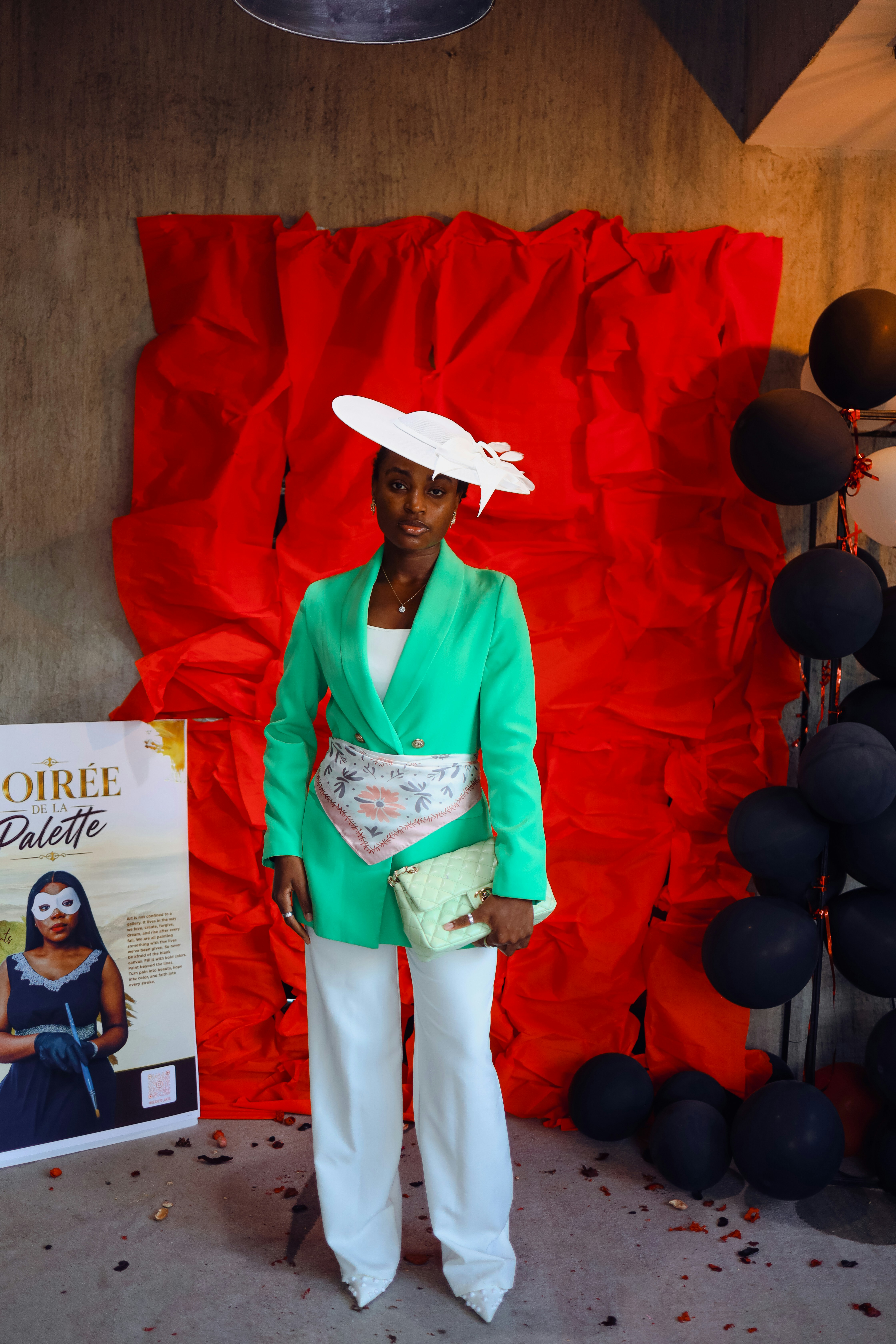 A woman in a green blazer and white hat standing before a red backdrop