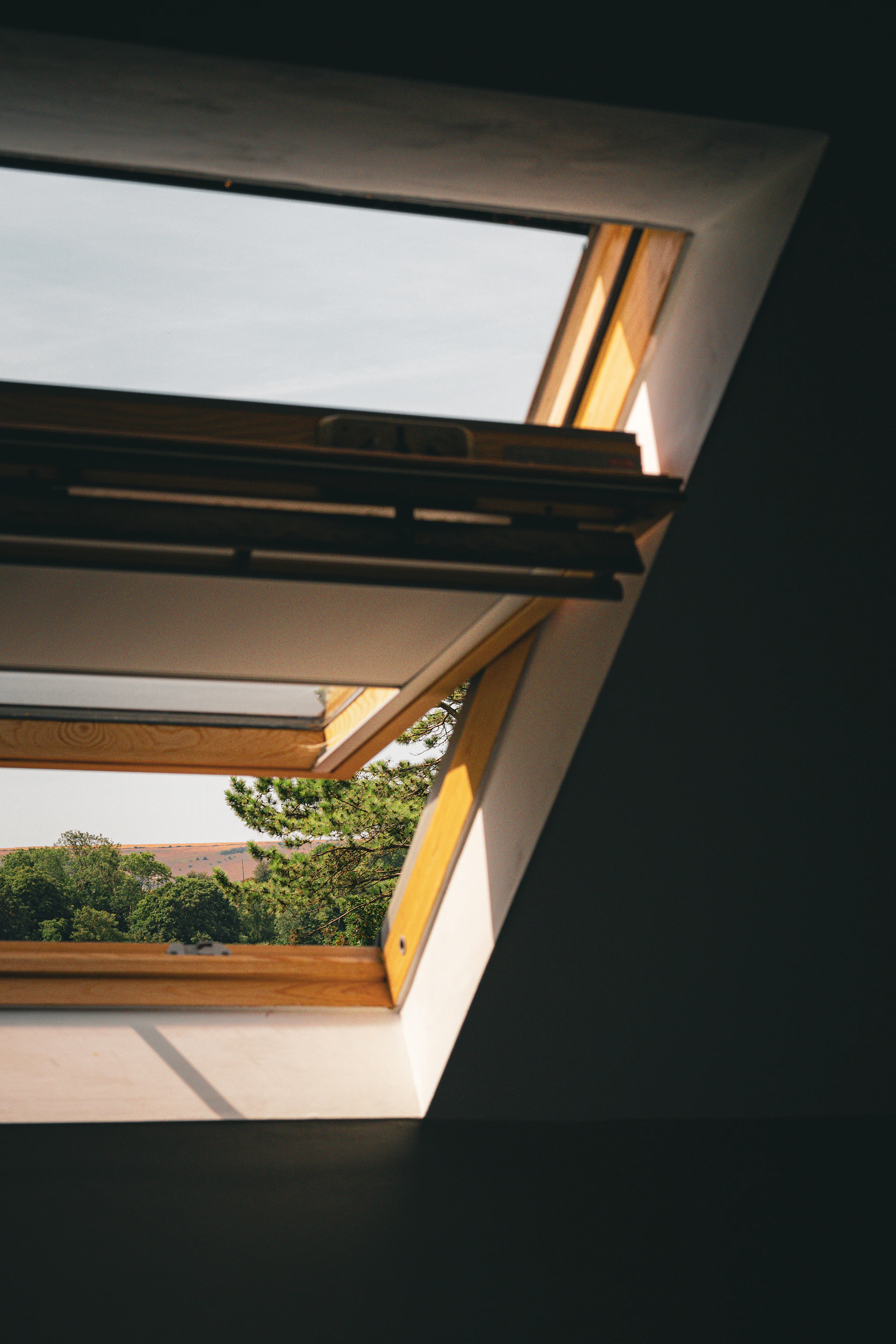 A wooden skylight window open to a view of green trees and hills