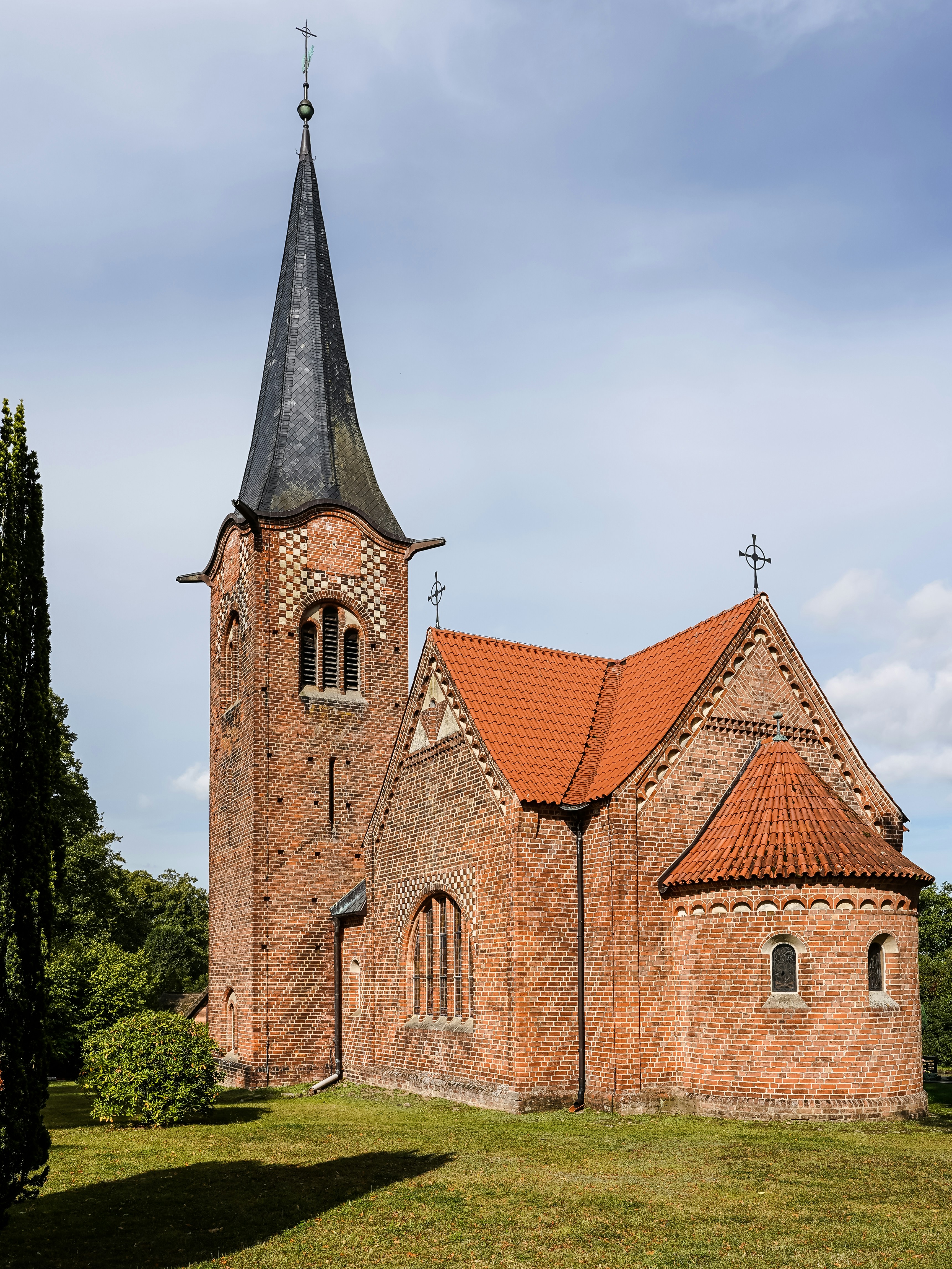 A red brick church with a tall steeple and tiled roof in a garden