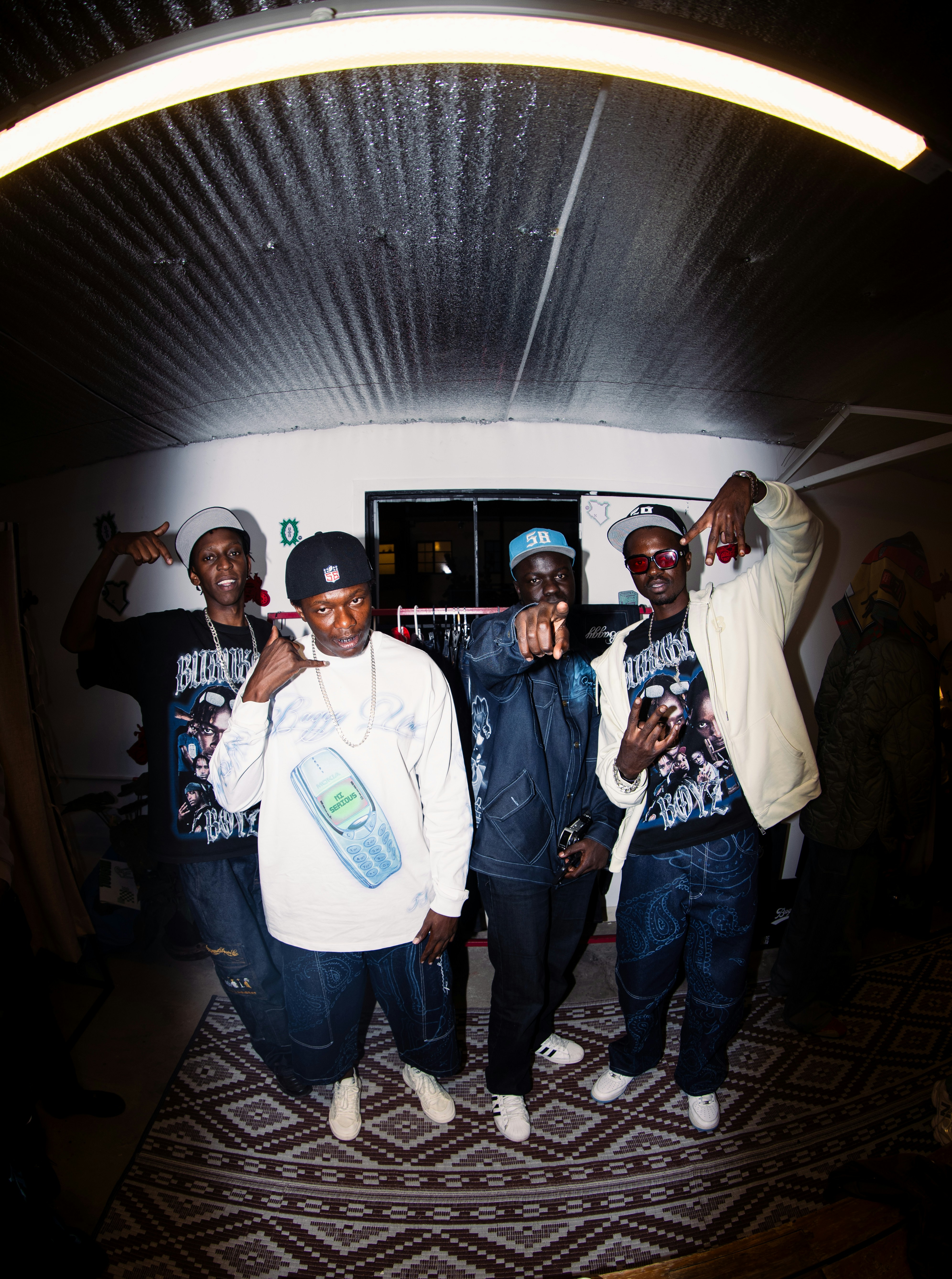 Four men posing in a room with a patterned rug and clothing rack