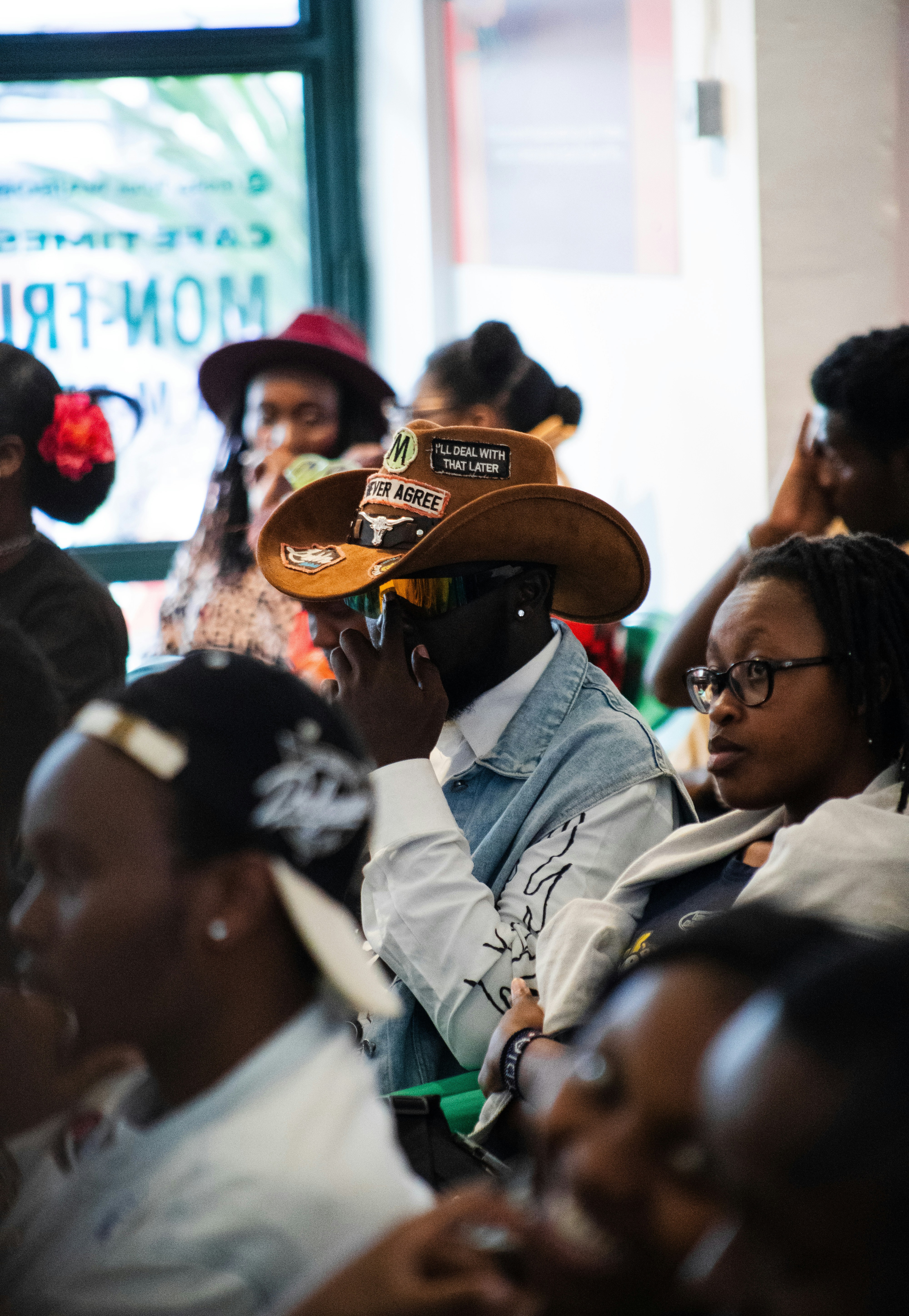 A person wearing a brown cowboy hat with patches in a crowded room