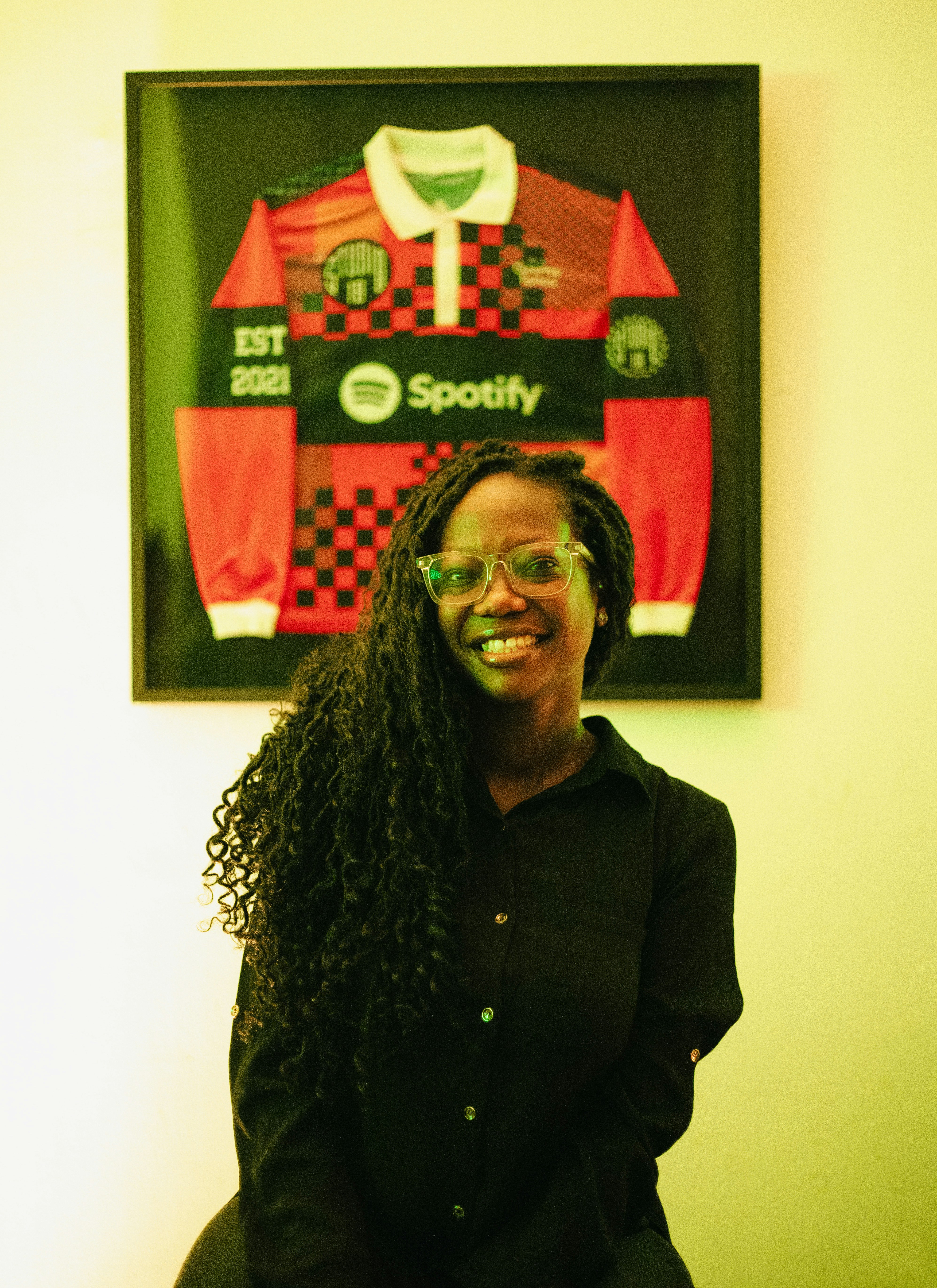A woman with long dark hair and glasses in front of a framed jersey