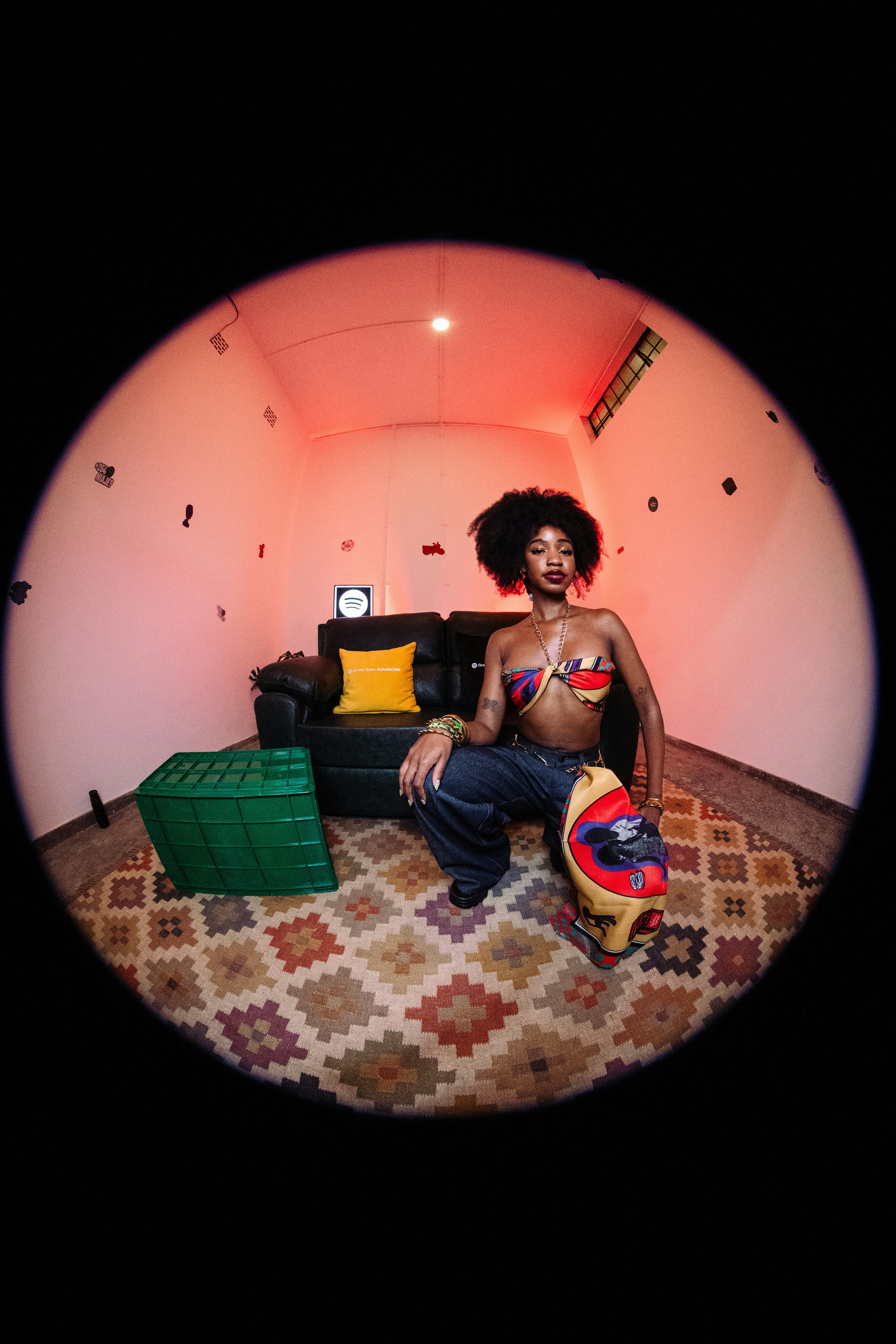 A person with an afro crouching on a patterned rug in a red-lit room