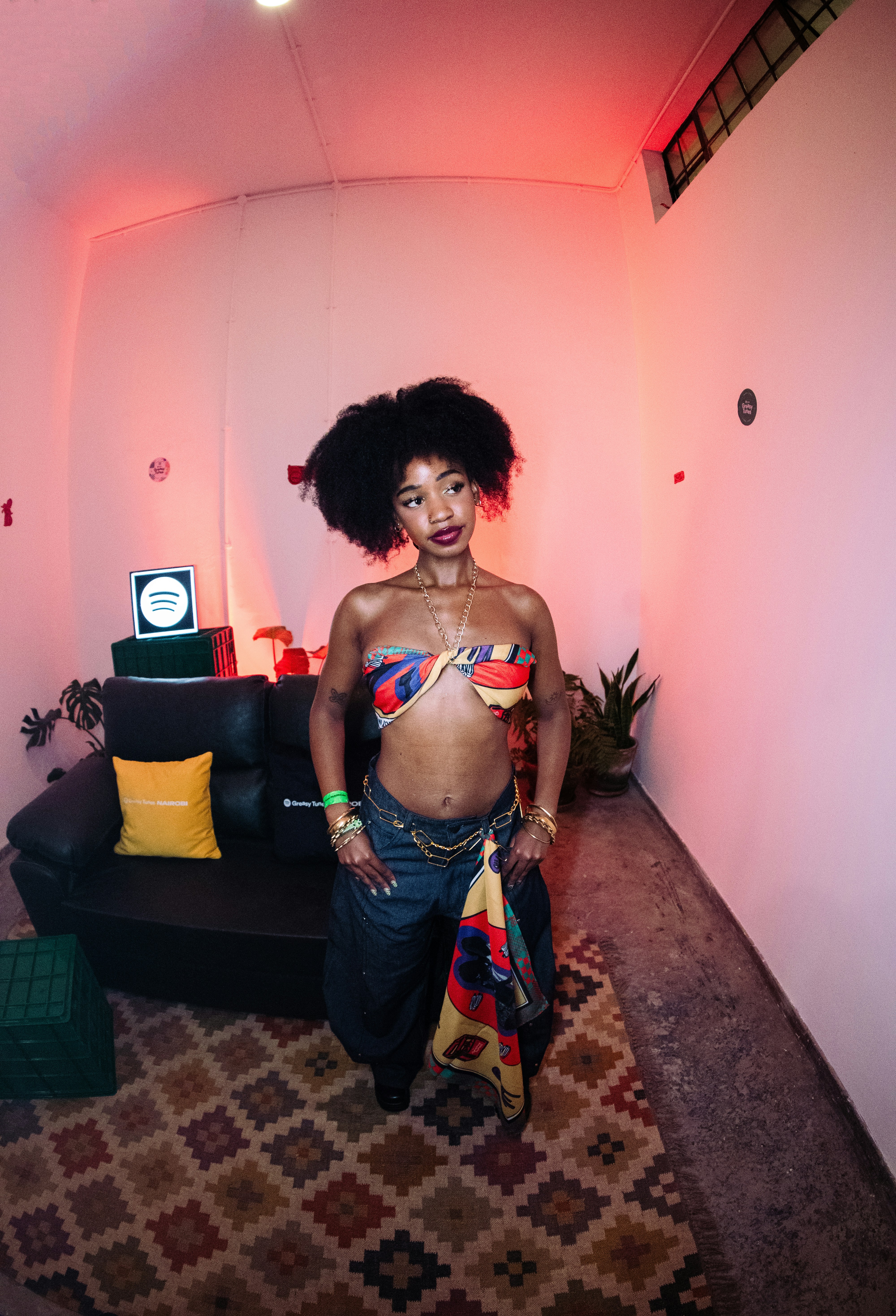 A woman with an afro in a colorful tube top and jeans in a room