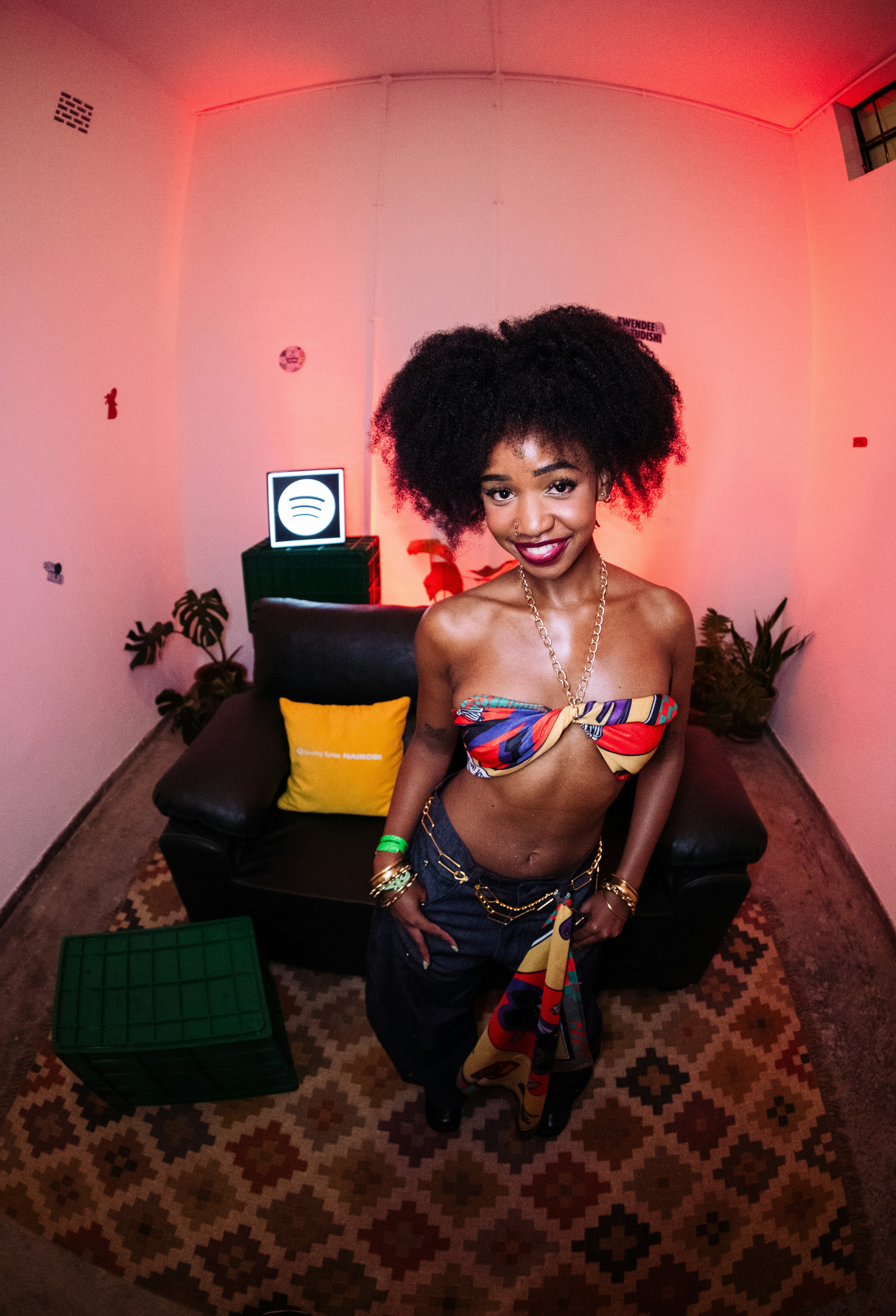 A woman with an afro wearing a colorful scarf top and jeans in a room