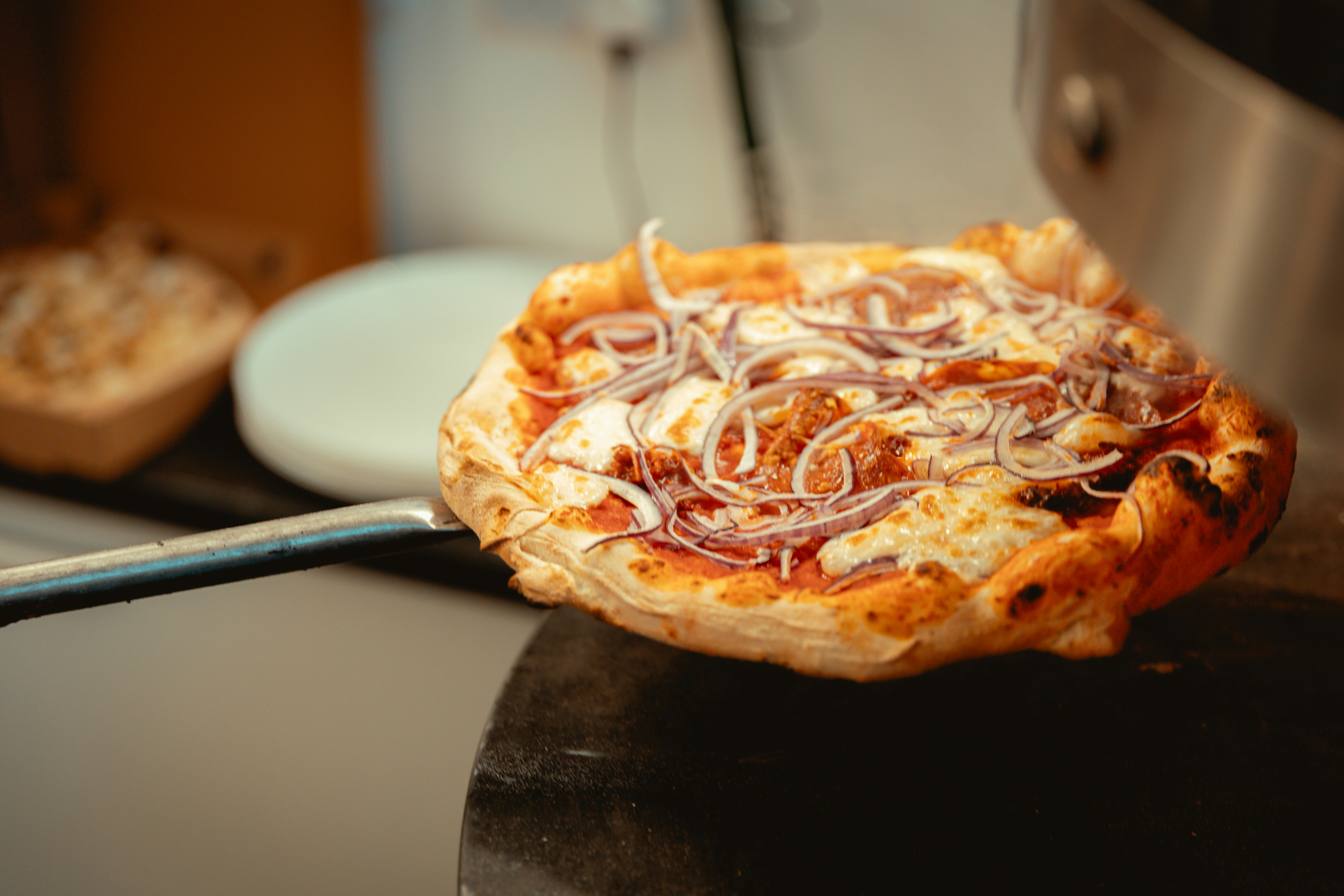 Pizza with red onion and melted cheese on a peel