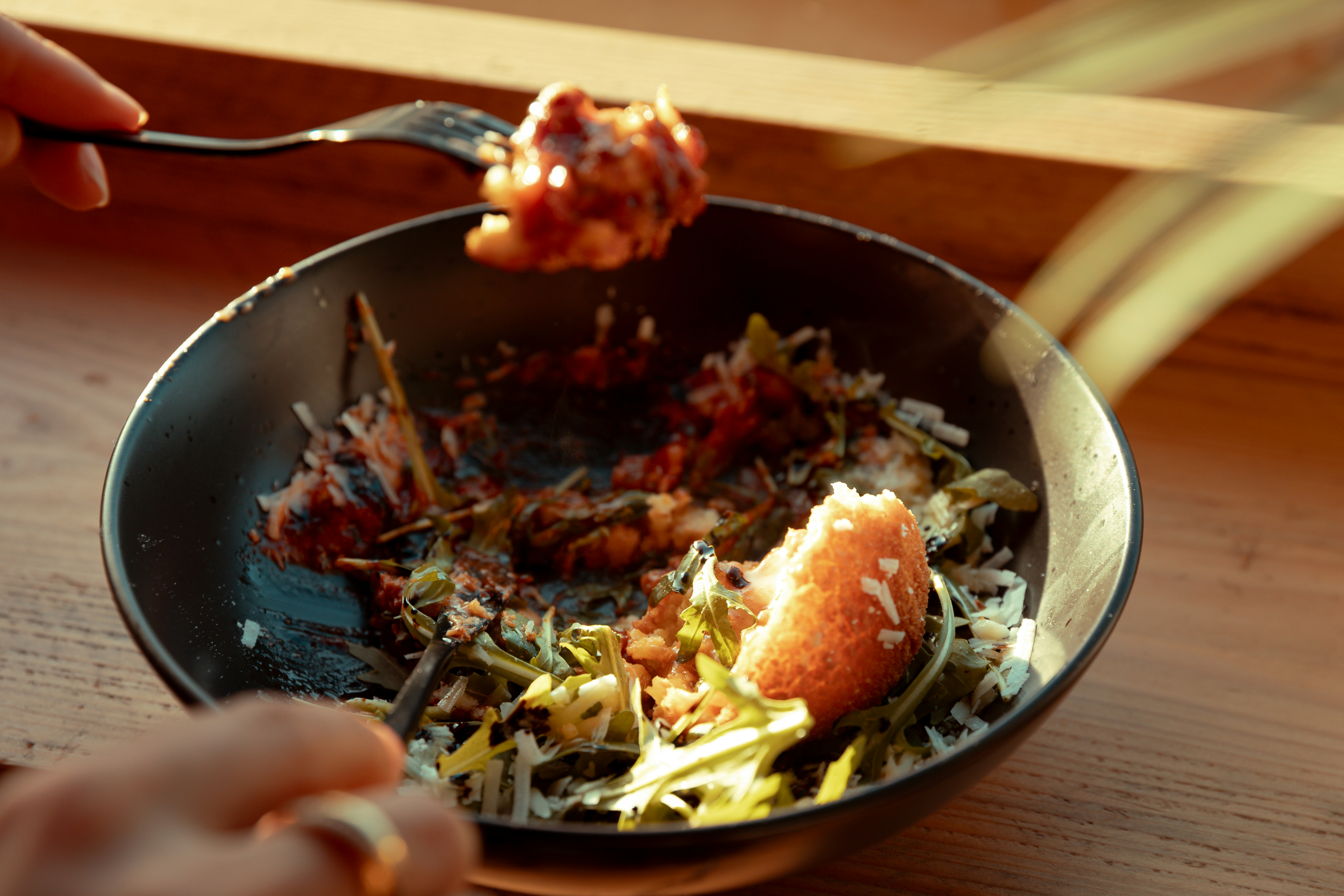 A person eating a salad with arugula and bread from a black bowl