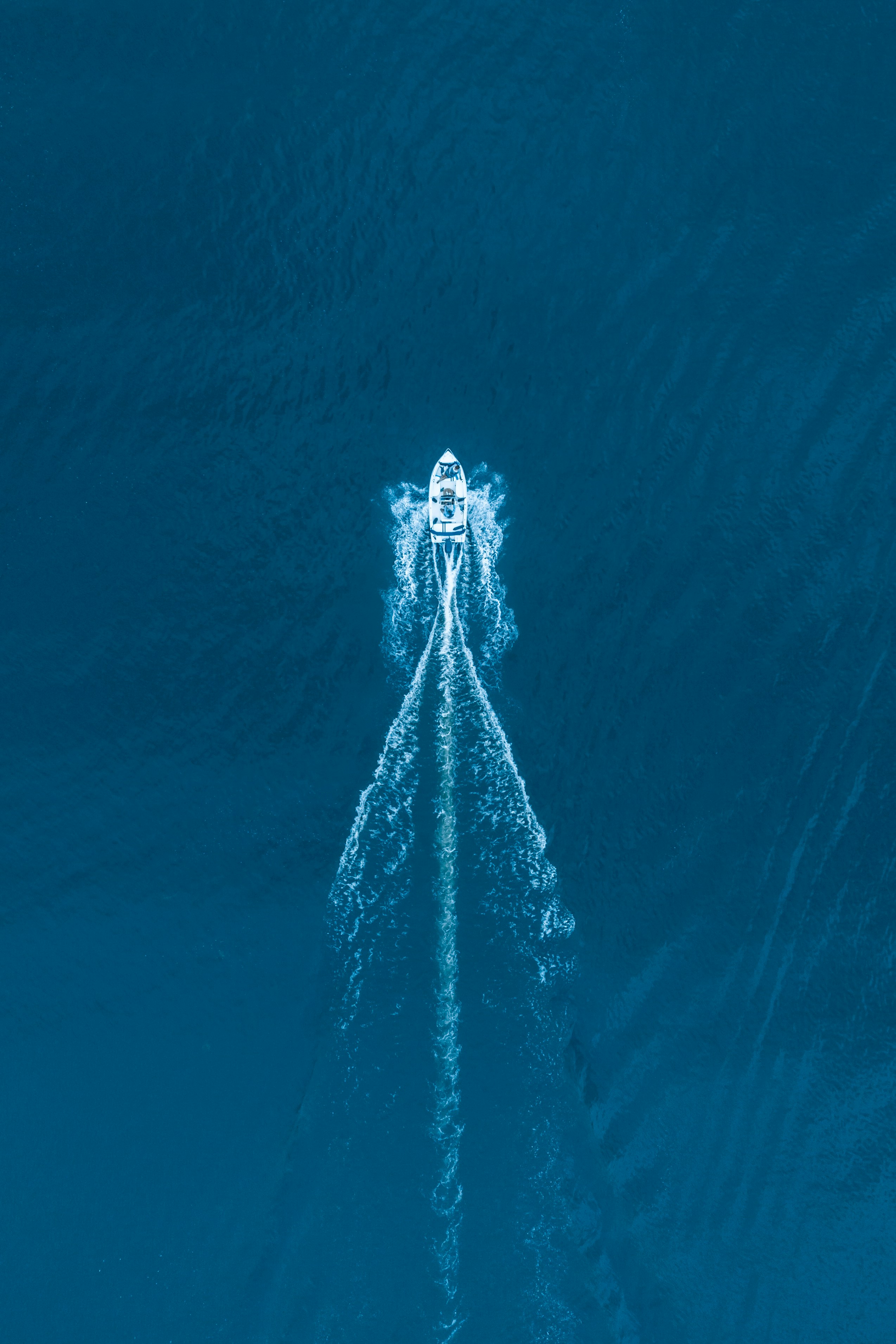 Um pequeno barco a motor branco se movendo por águas azul-profundas deixando um rastro branco