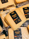 Blocks of yellow cheese in plastic packaging with black labels on a shelf