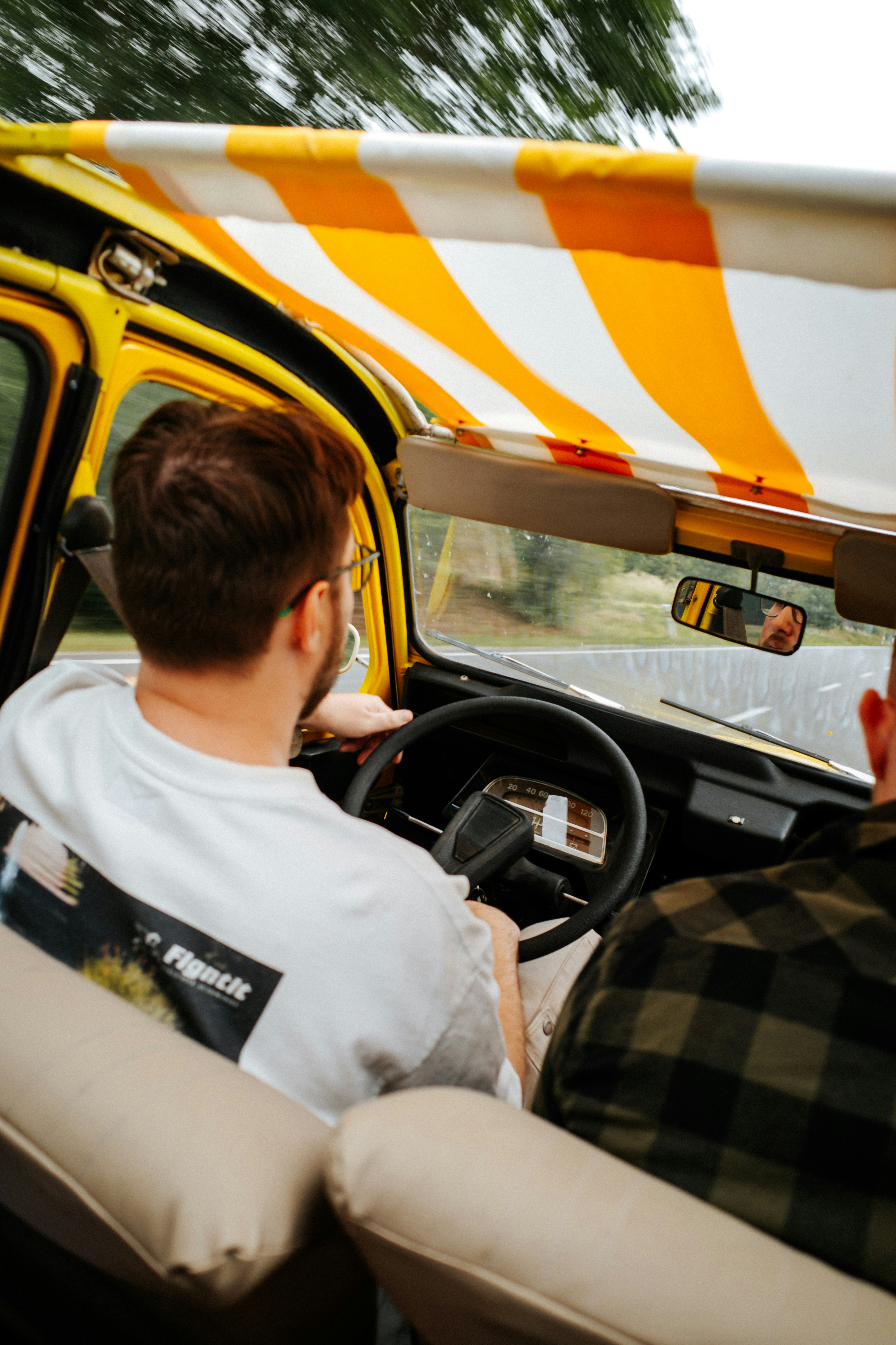 Una persona che guida un'auto gialla con il tetto a righe su una strada