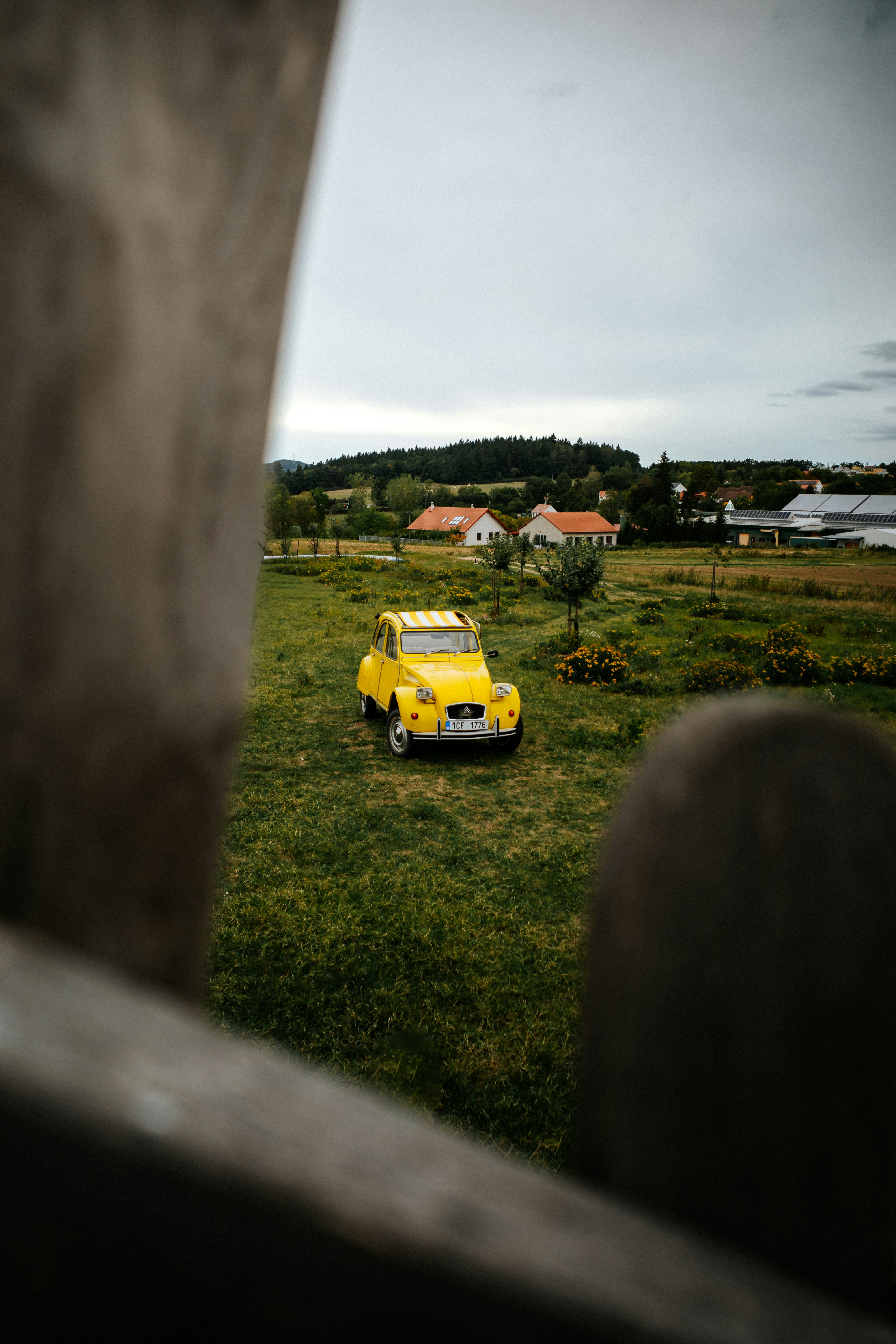 Una Citroën 2CV gialla parcheggiata in un campo erboso sotto un cielo nuvoloso