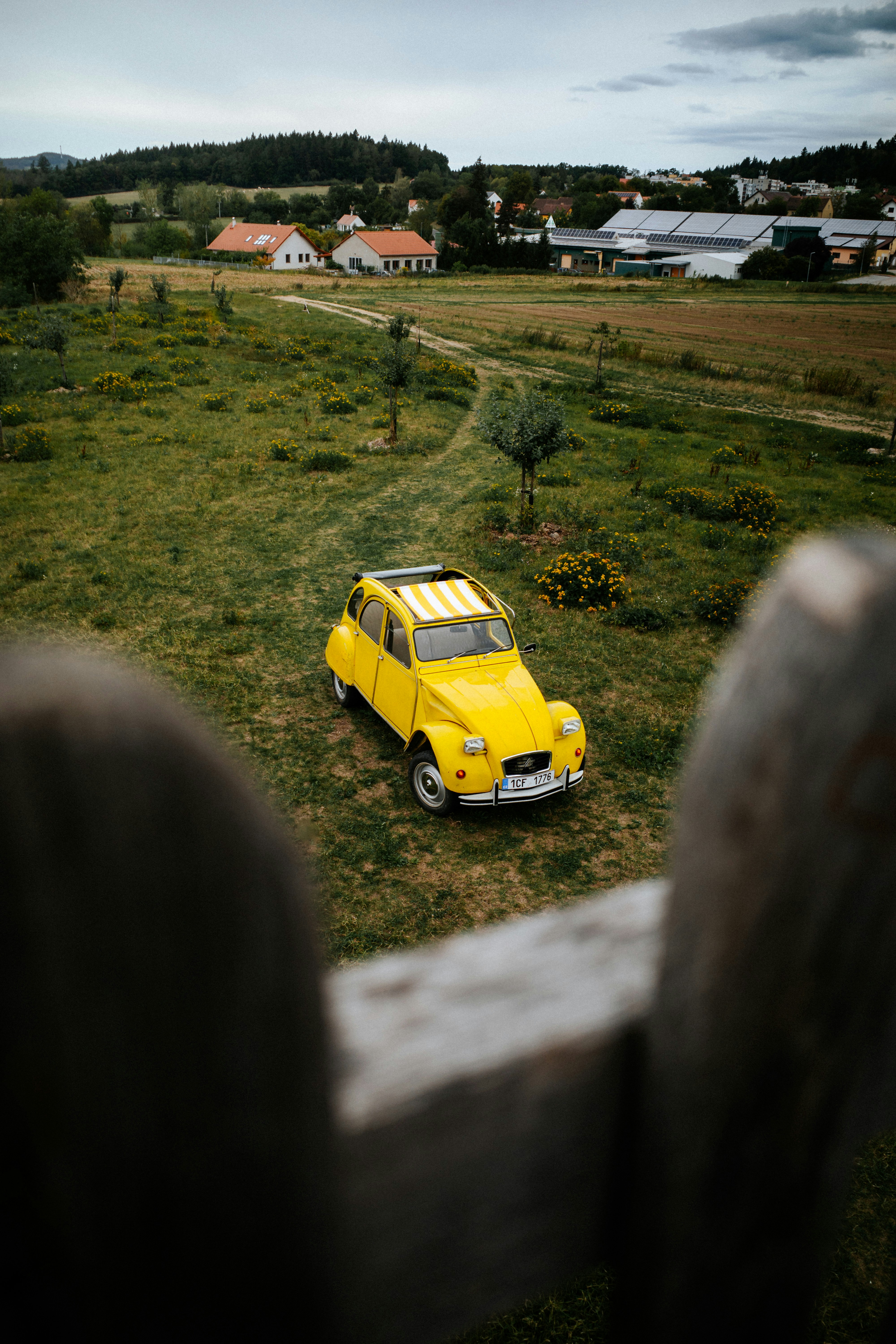 Una Citroën 2CV gialla parcheggiata in un campo erboso vicino a un villaggio rurale