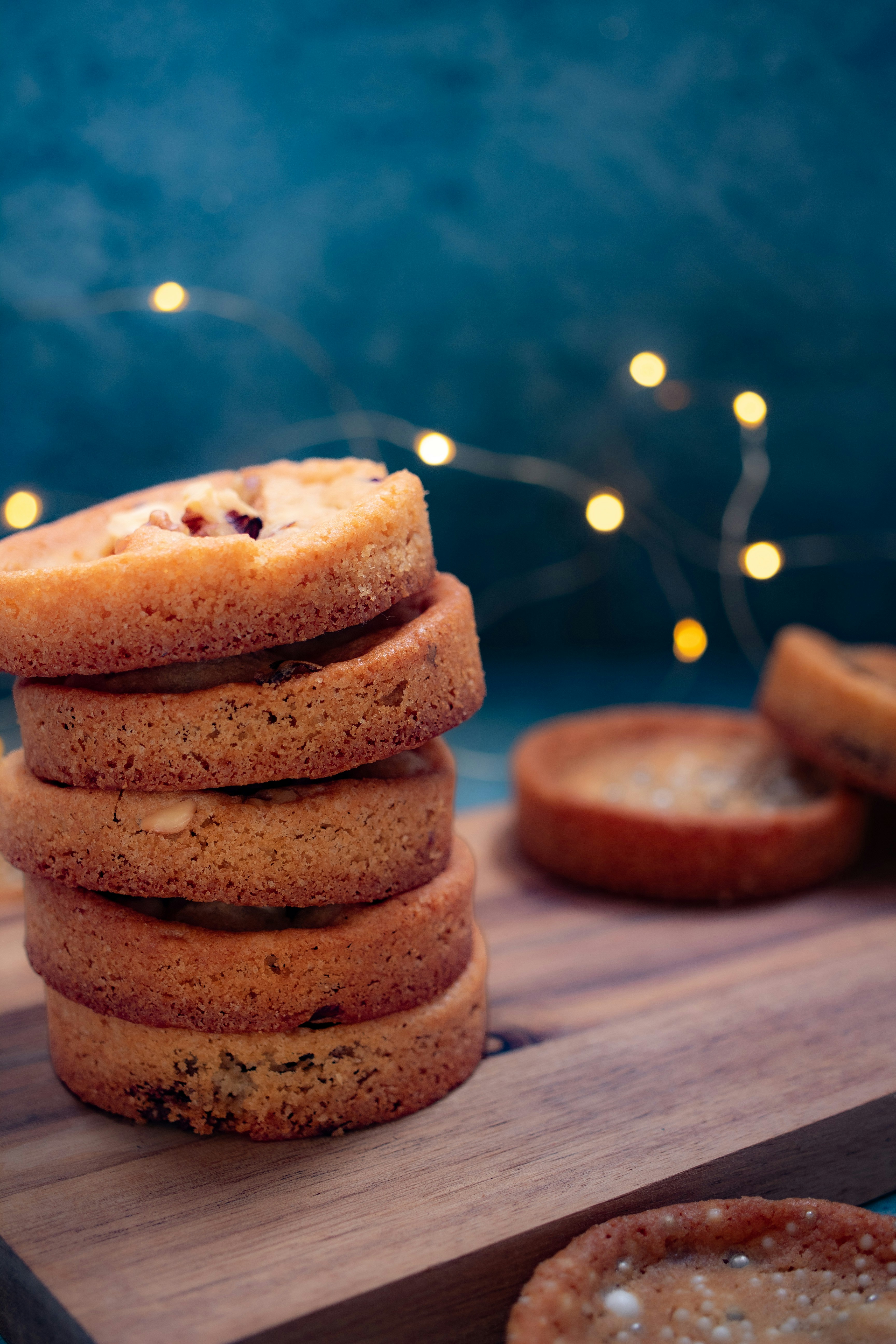 A stack of round cookies on a wooden board with blurred fairy lights