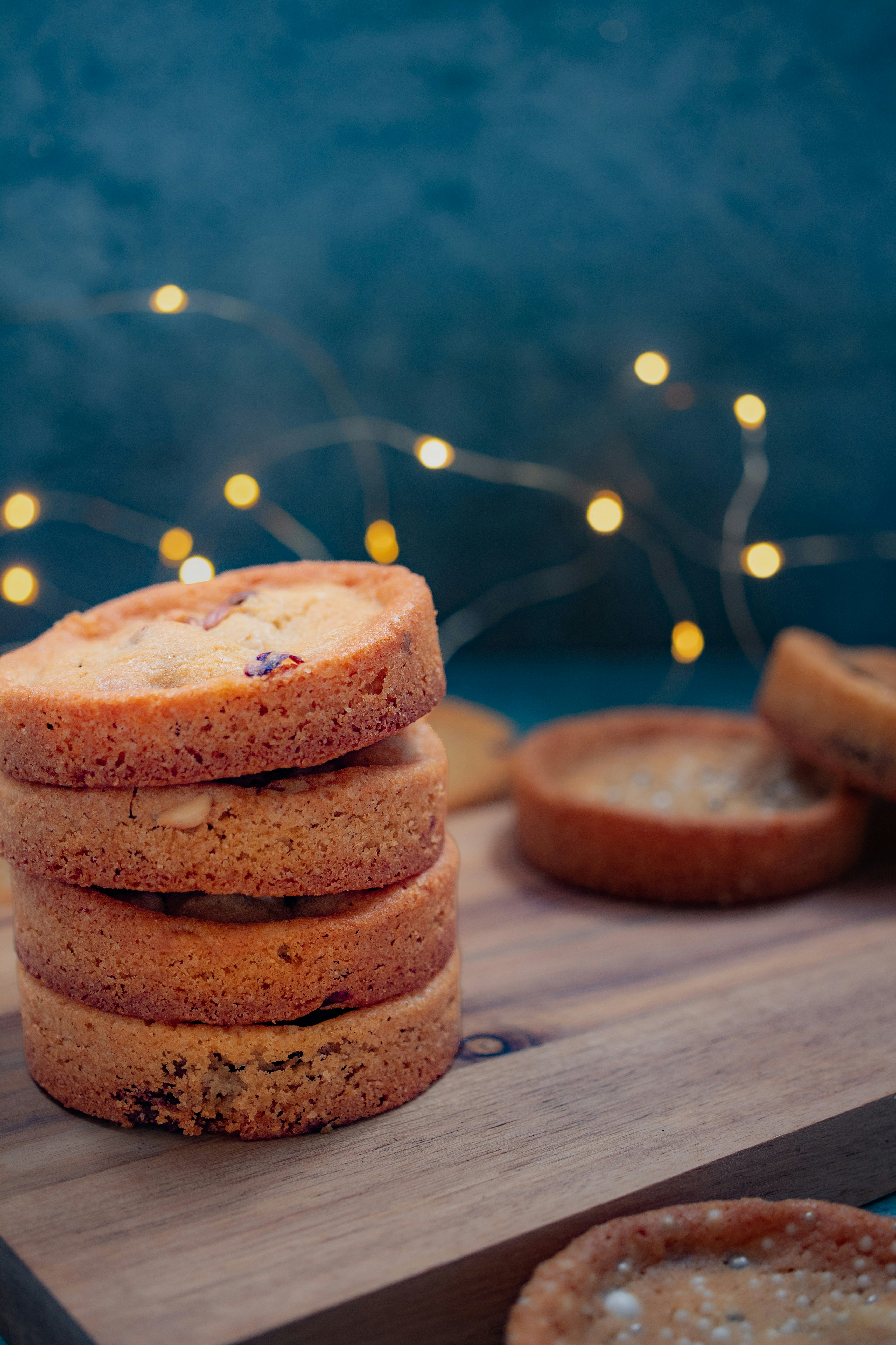 A stack of four round cookies on a wooden board with bokeh fairy lights