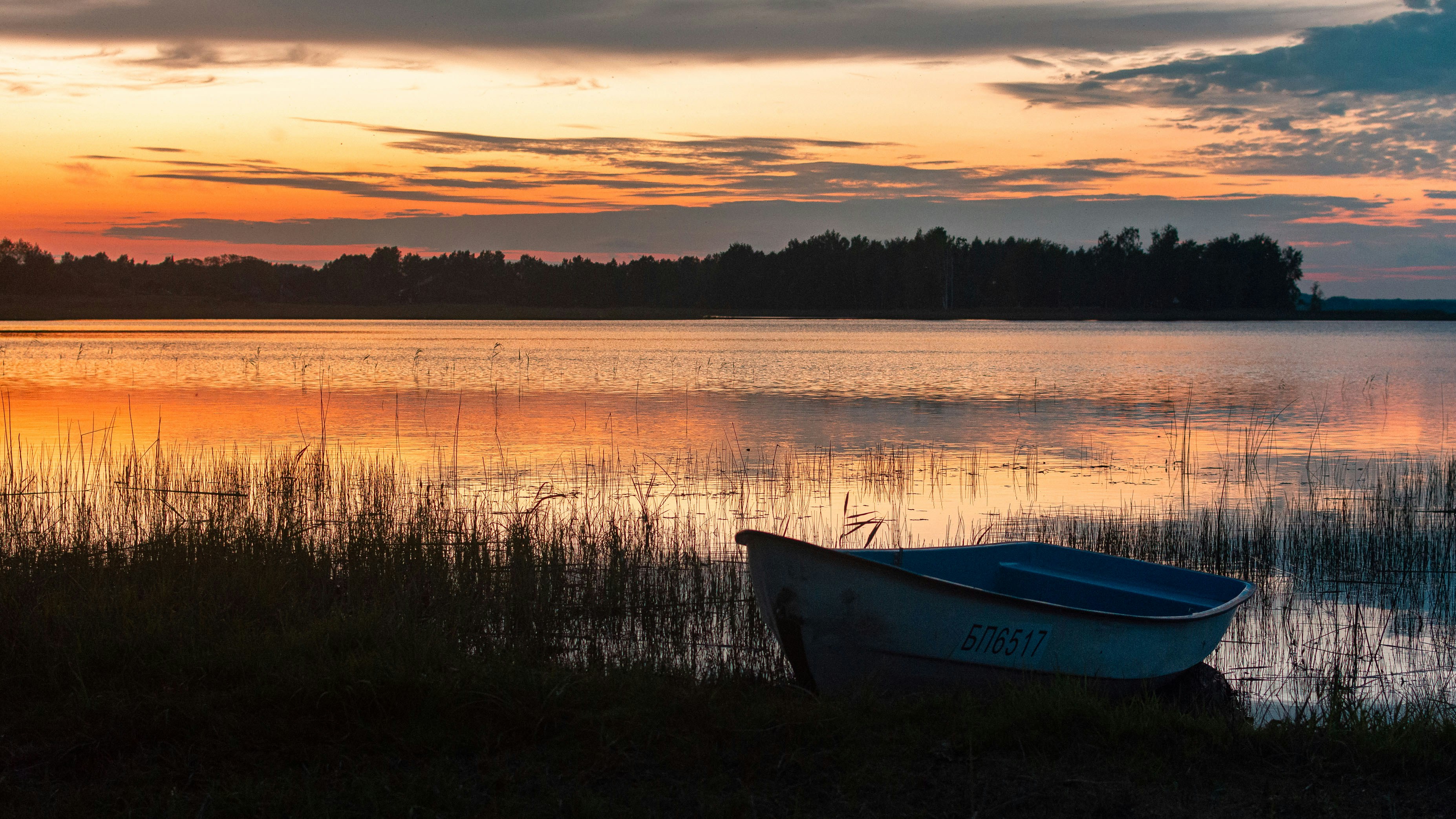 A small boat on the shore of a lake under a warm orange sky