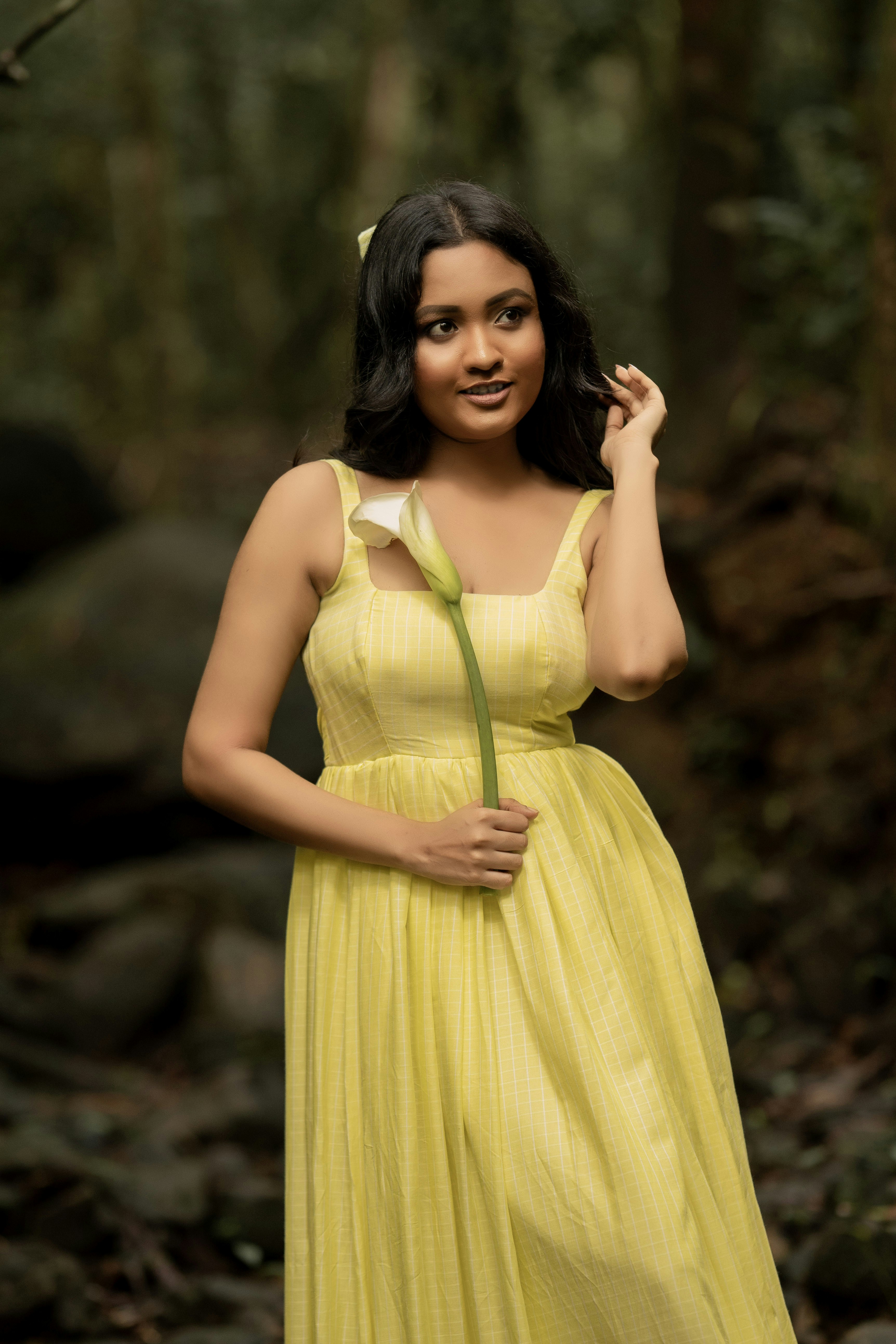 A woman in a yellow plaid dress holding a white calla lily outdoors