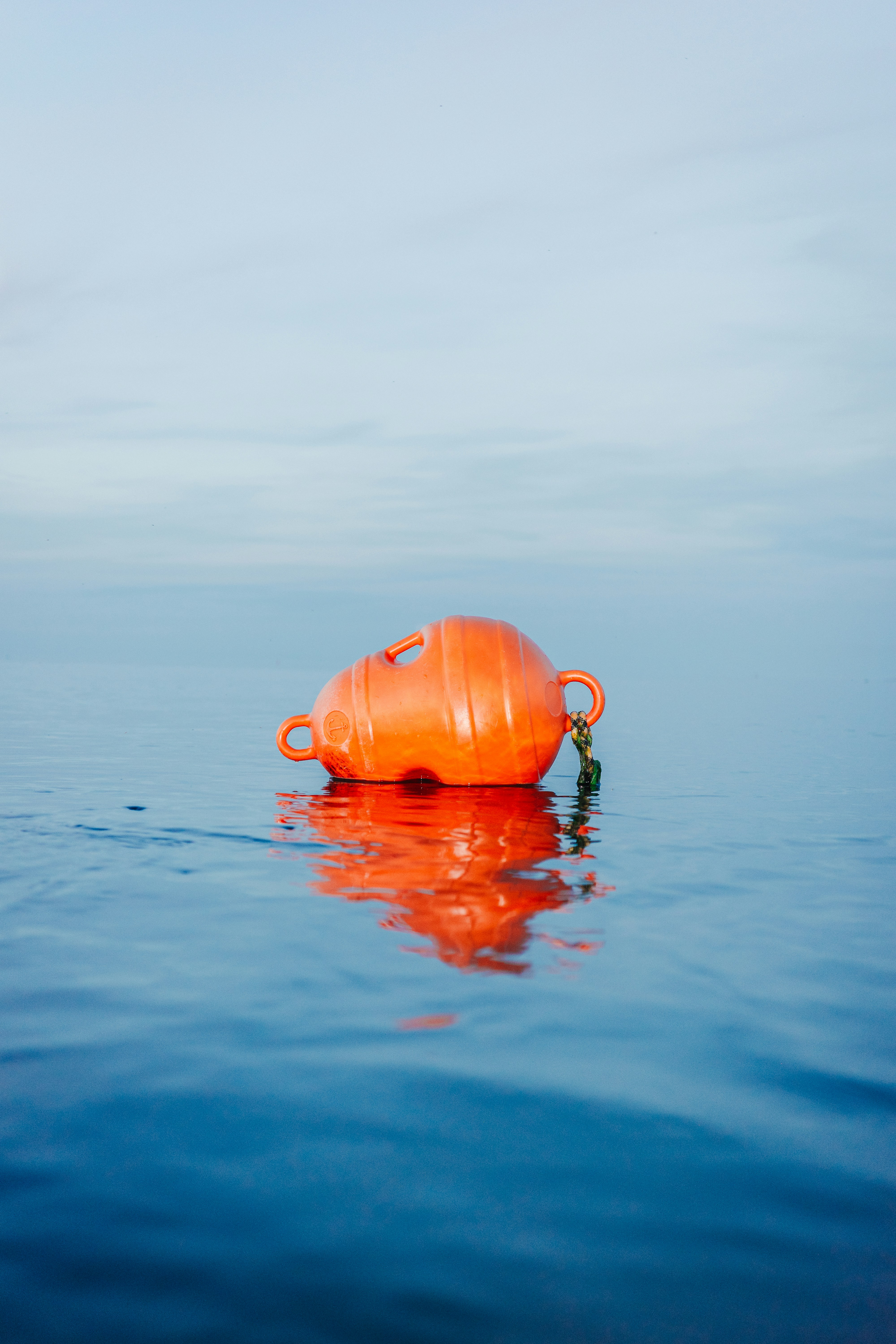An orange plastic buoy floating on calm blue water with a clear reflection