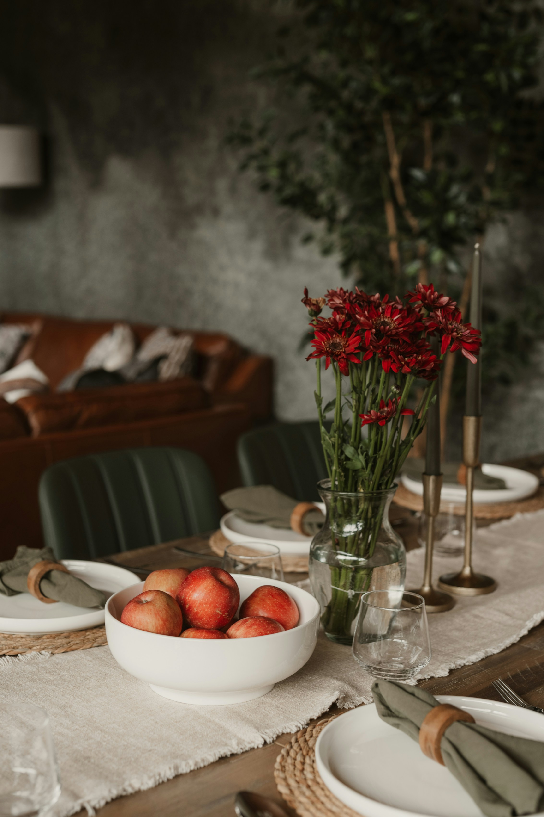 A bowl of red apples and a vase of red flowers on a dining table