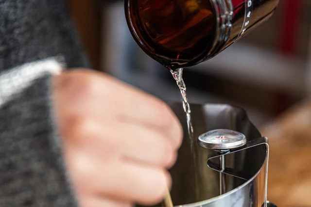 Fragrance oil being poured from a brown glass bottle into a metal pouring pitcher
