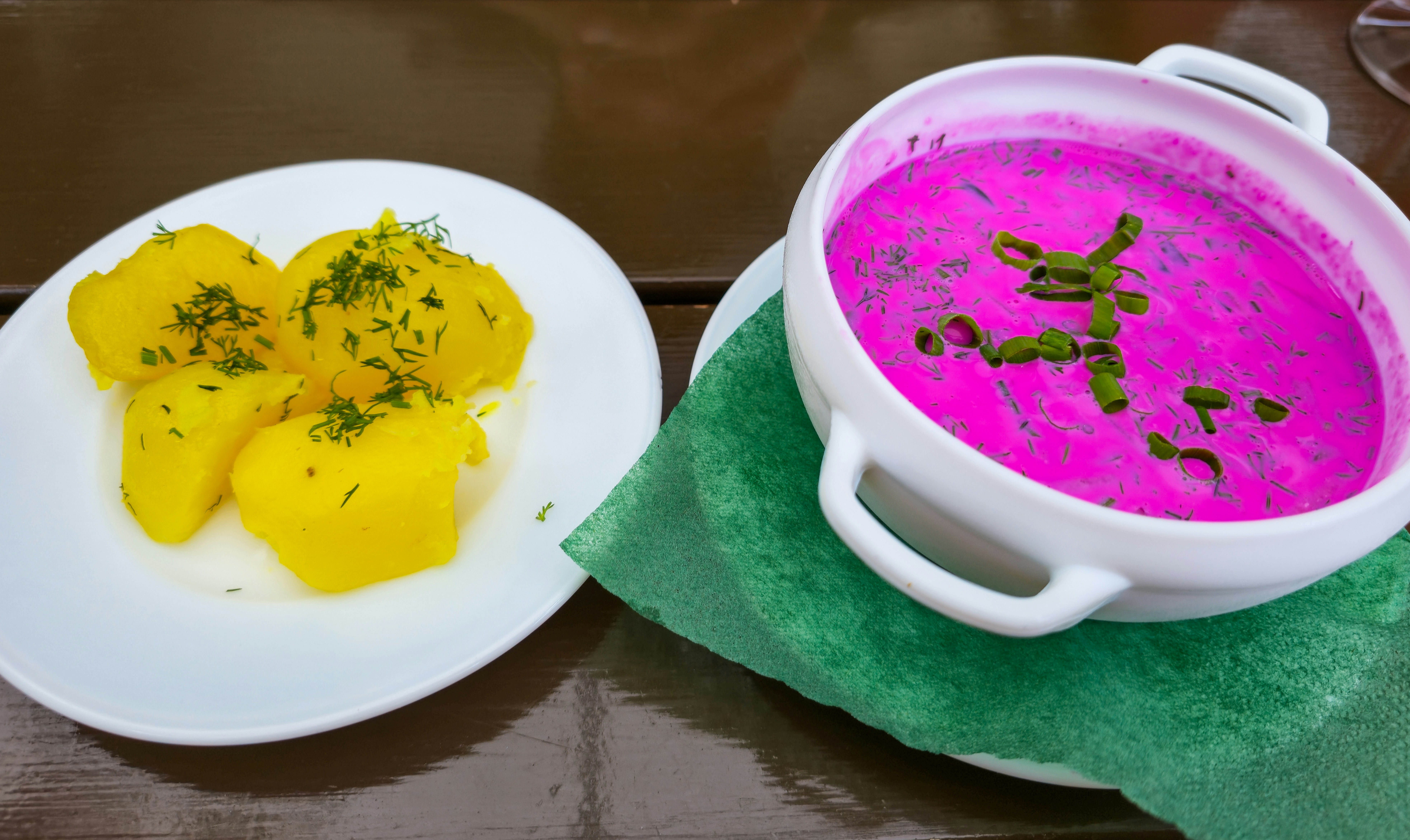 Una ciotola di zuppa fredda di barbabietole rosa acceso accanto a patate gialle bollite con aneto