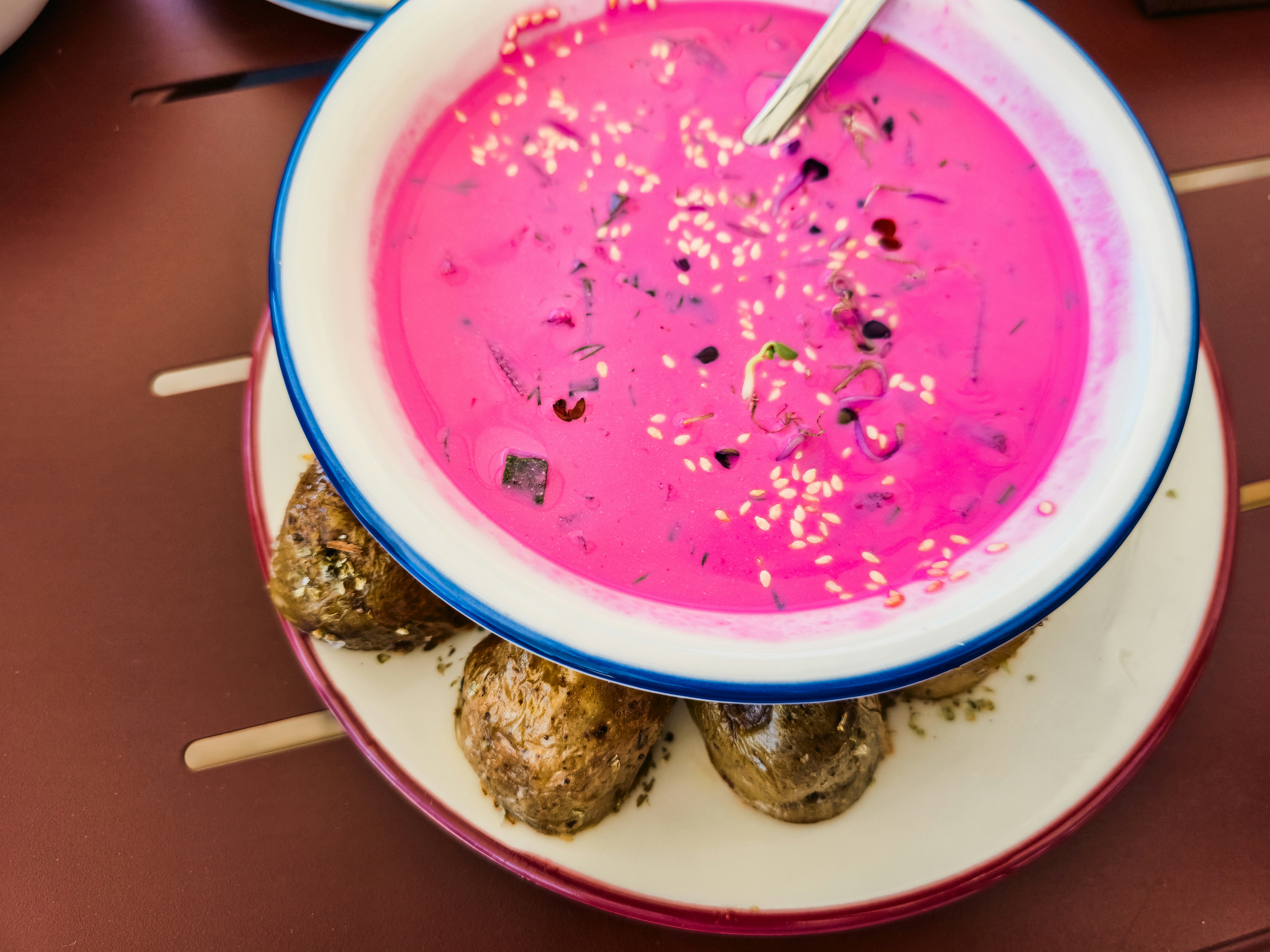 Una ciotola di zuppa di barbabietole rosa acceso con semi di sesamo e patate arrosto