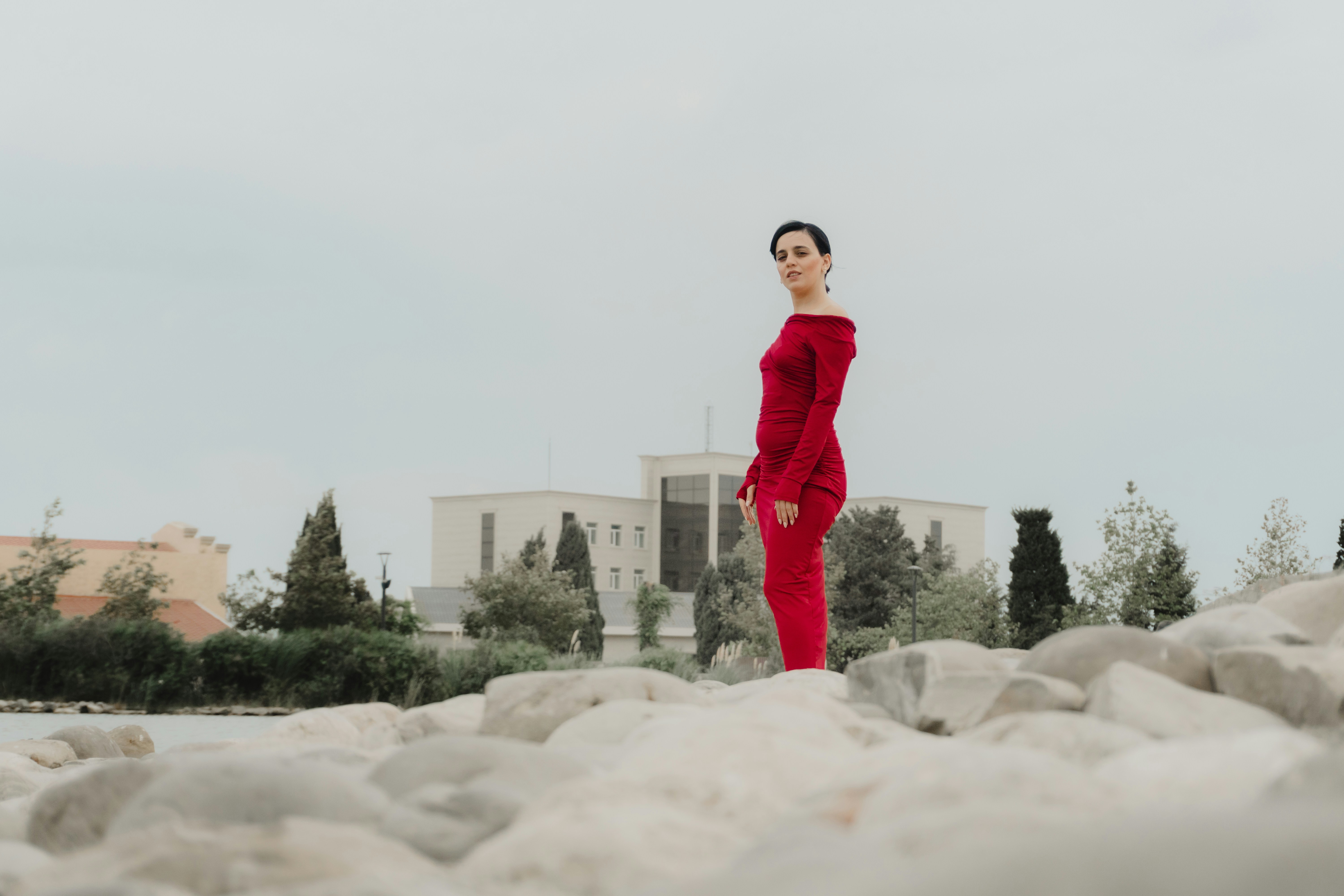 A woman in a long red dress standing on a rocky shore