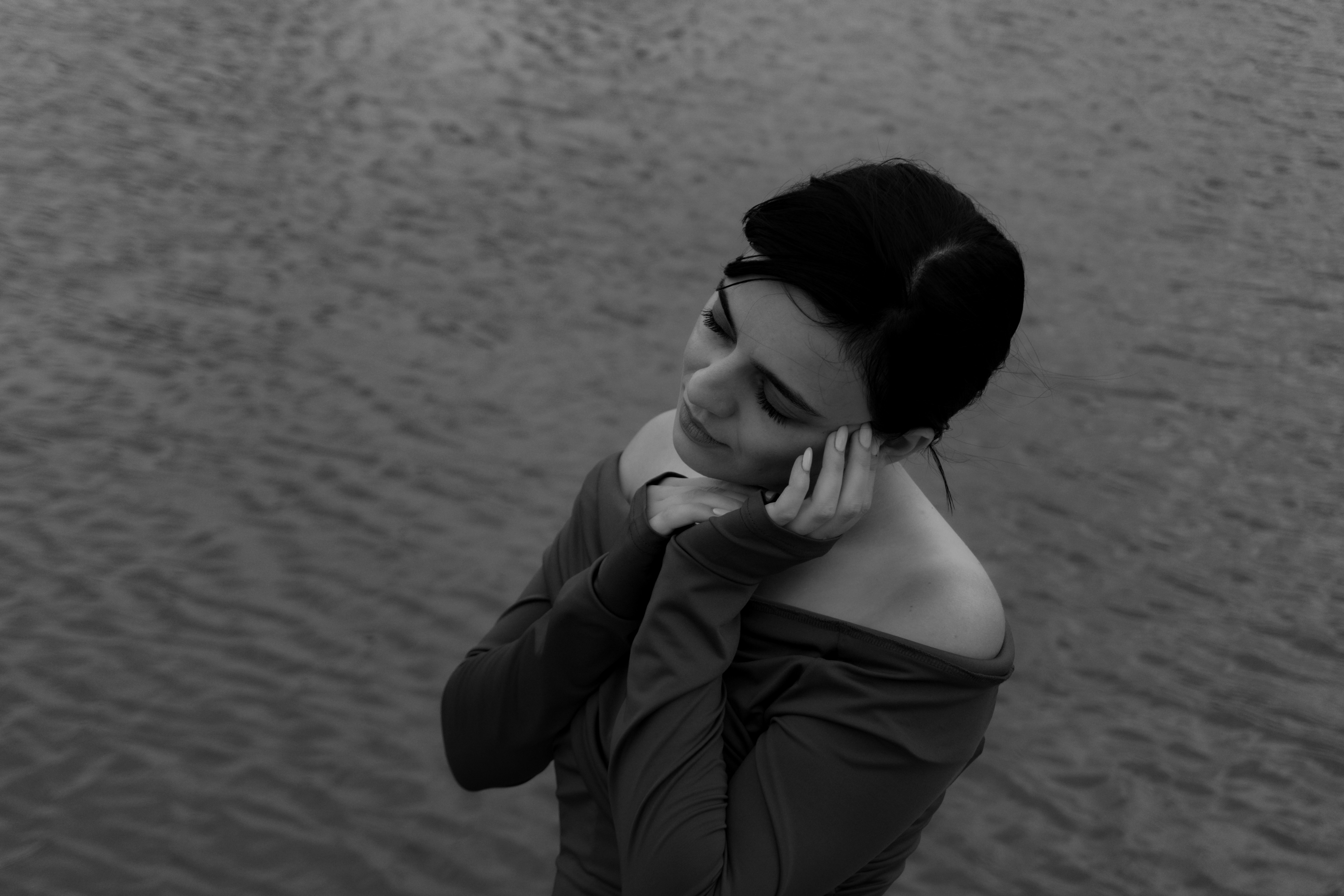 A woman in an off-the-shoulder top with hands near her face above water