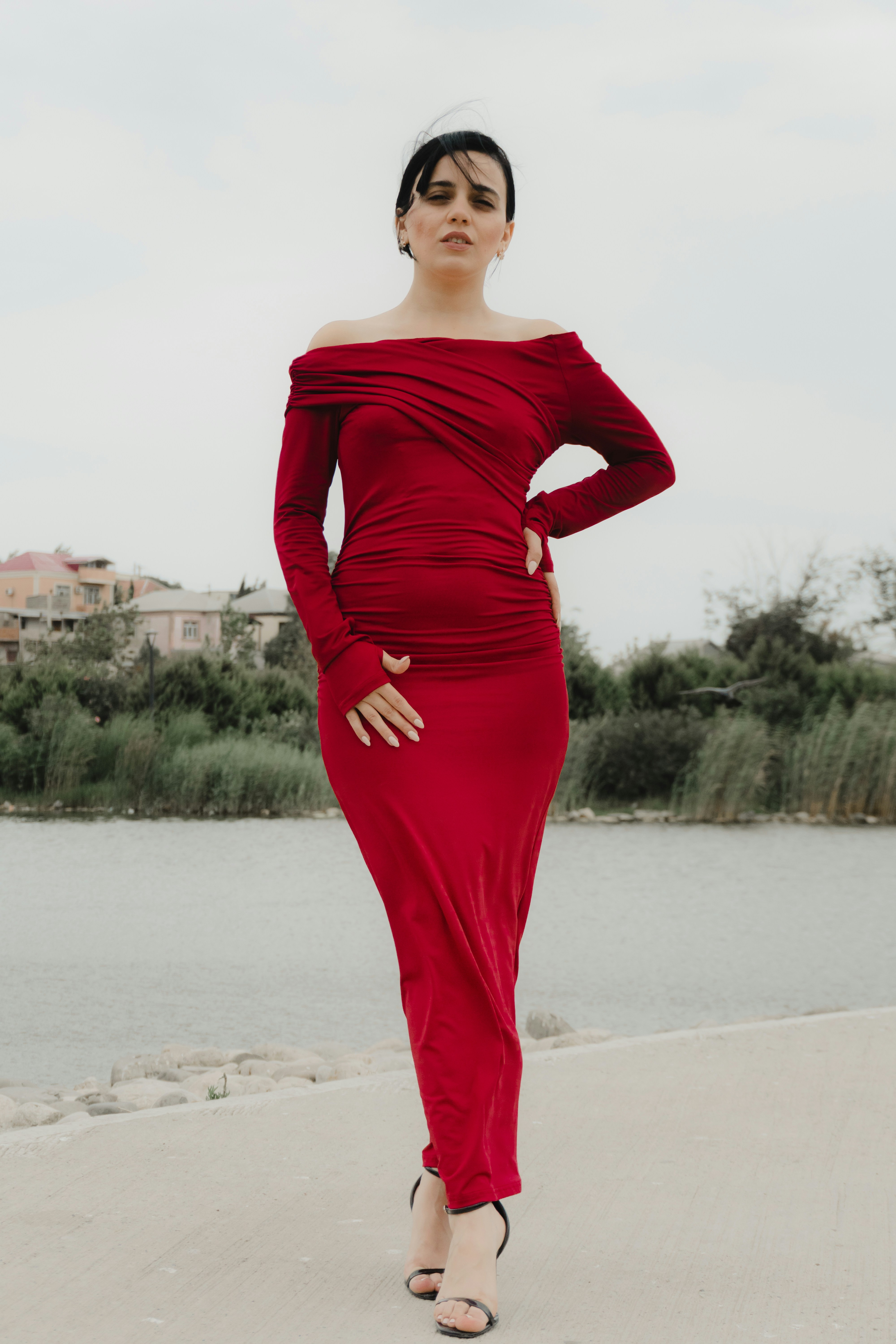 A woman in a long red off-the-shoulder dress by a lake