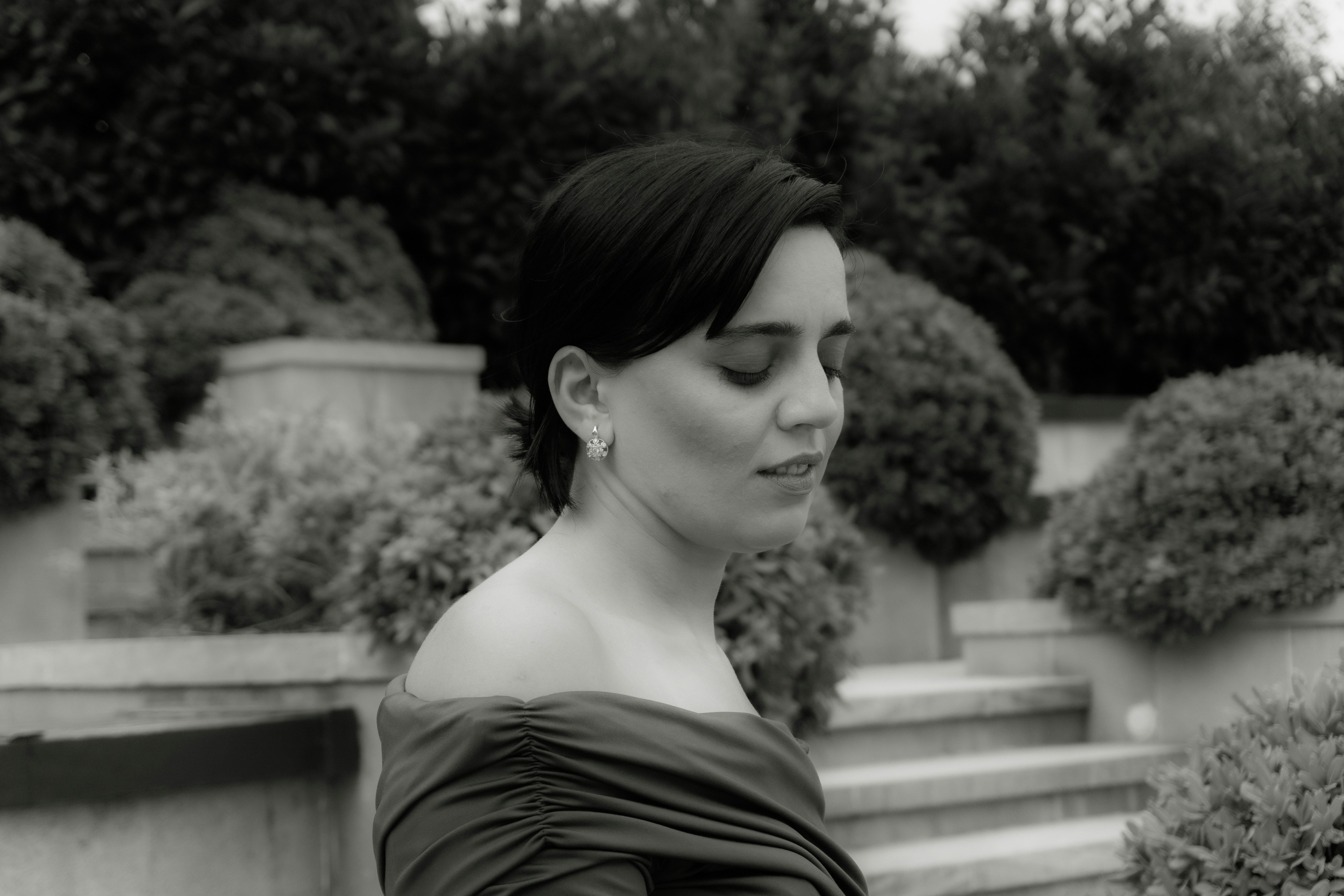 A woman in an off-the-shoulder dress with eyes closed in a garden