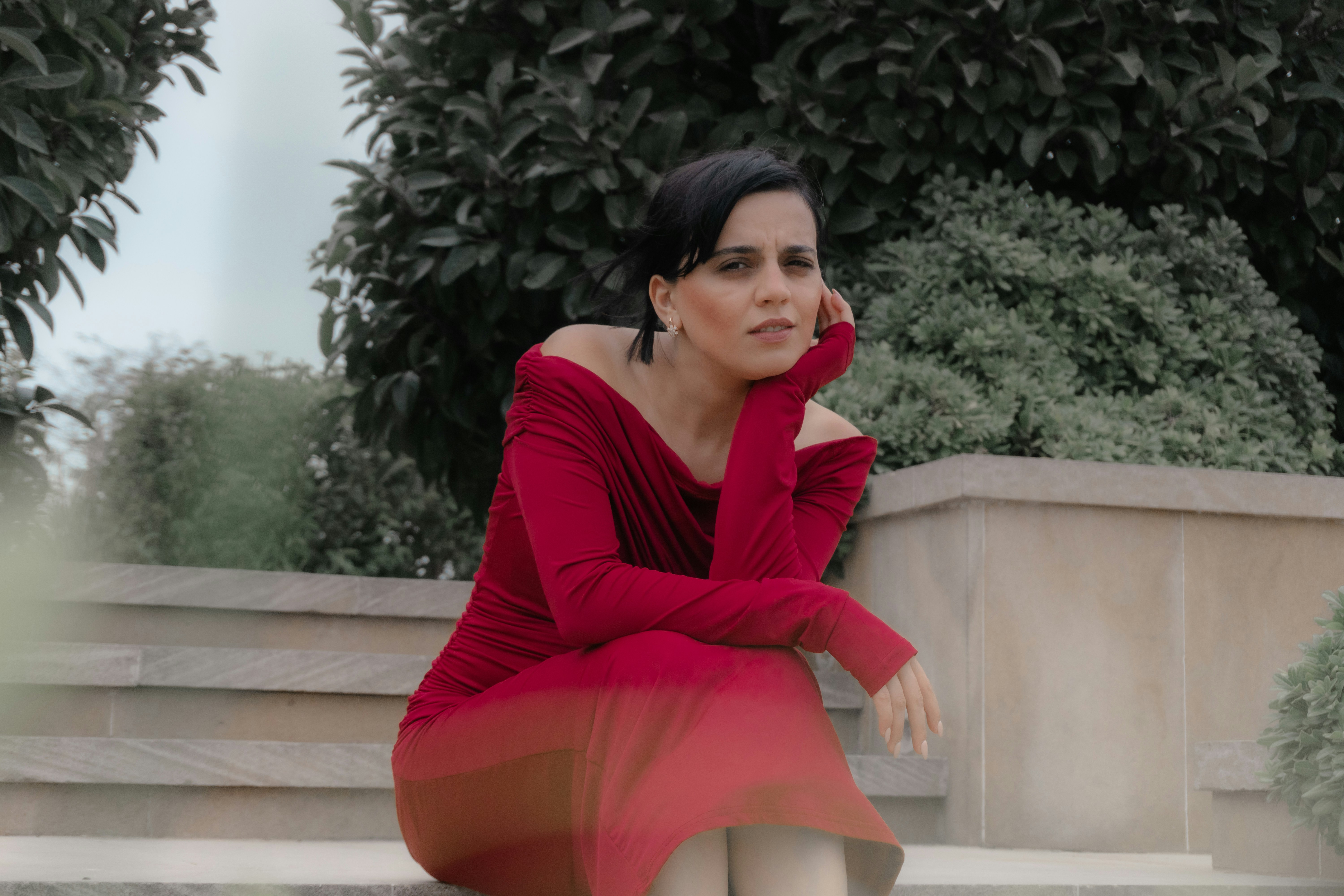 A woman in a red off-the-shoulder dress sitting on stone steps outdoors