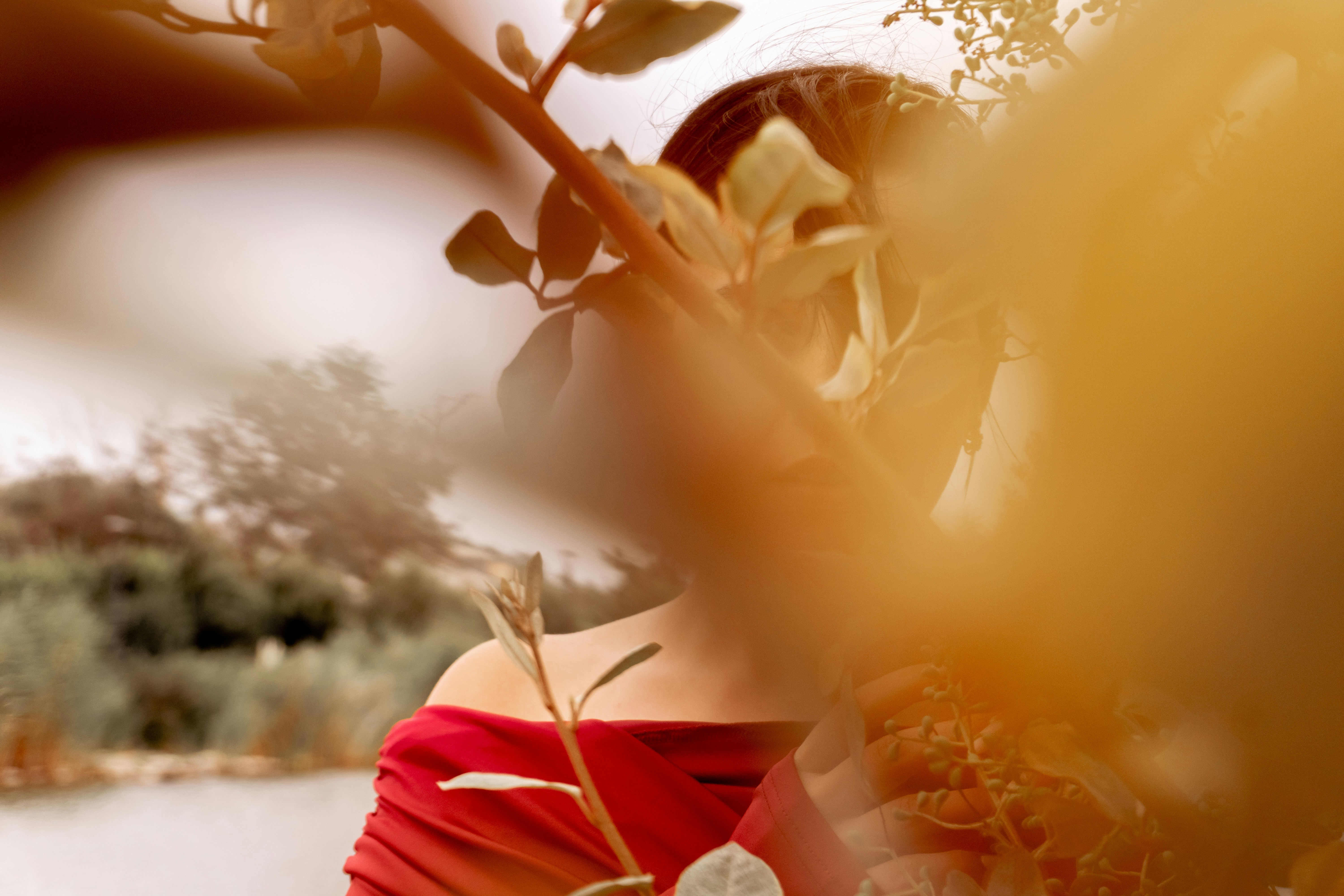 A person in a red off-the-shoulder top partially obscured by golden foliage