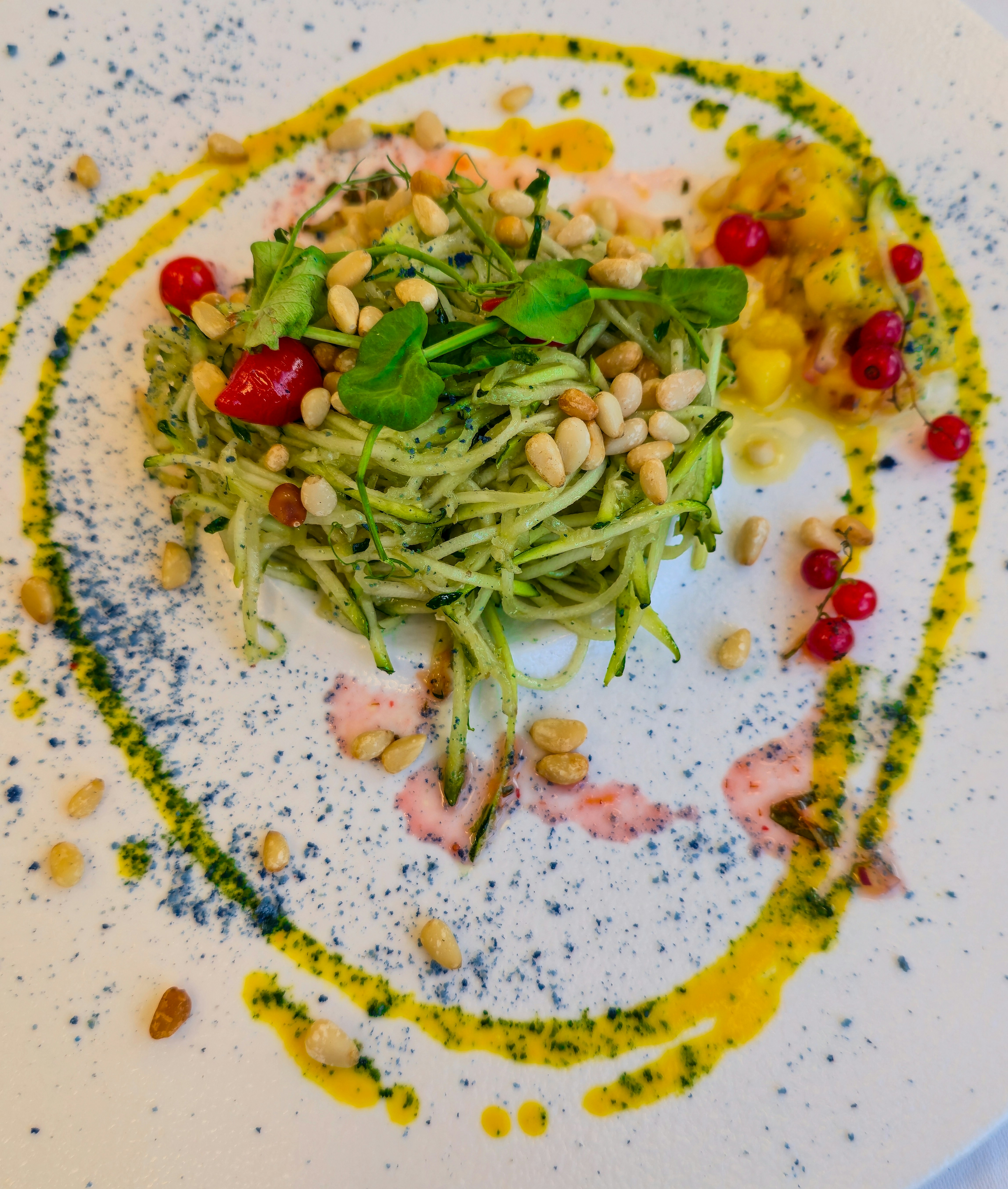Zucchini noodles with pine nuts, red currants, and herbs on a white plate